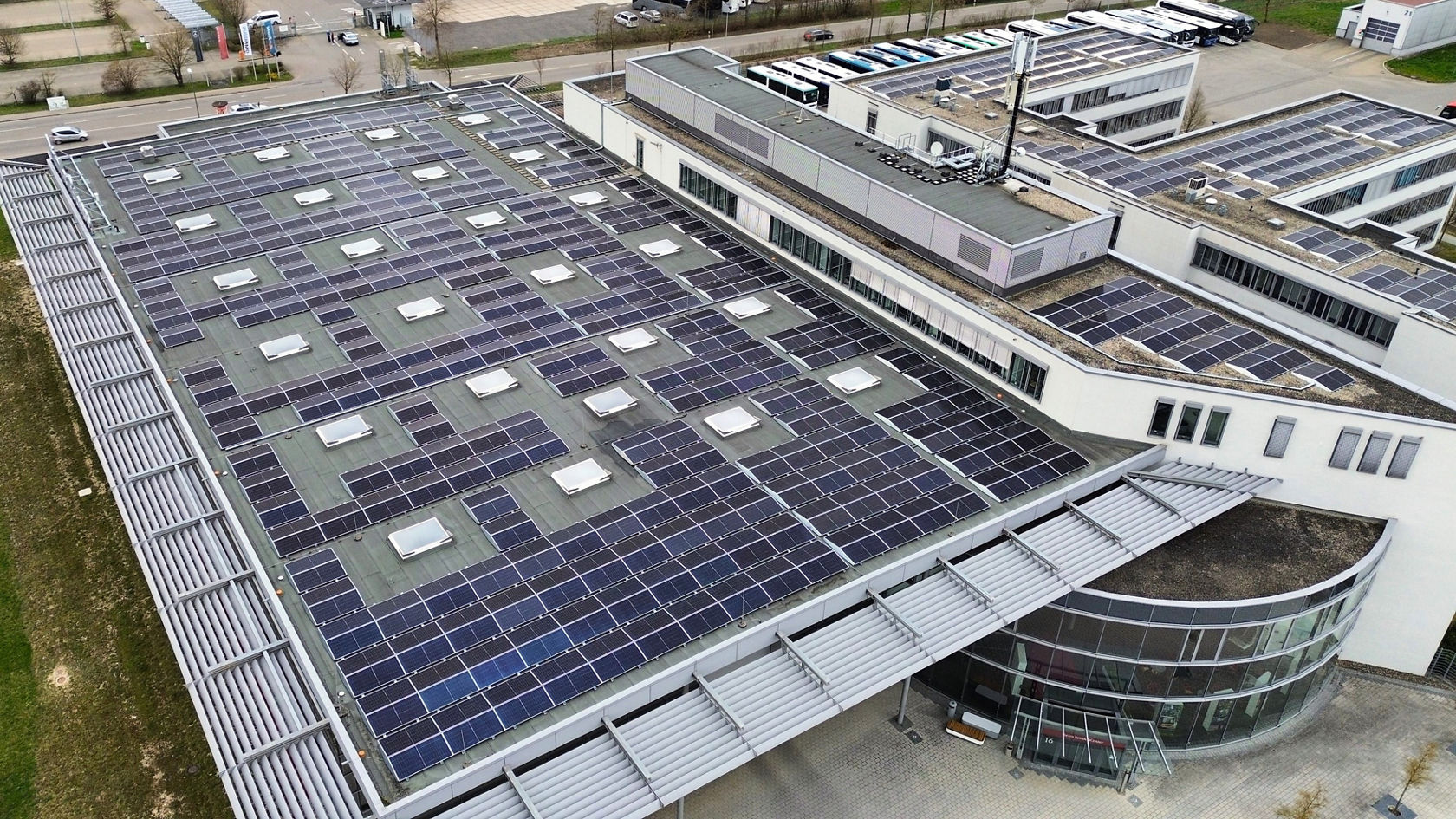 Aerial shot of the Daimler Buses site in Neu-Ulm with a large-scale photovoltaic system on the roofs and parked buses in the background