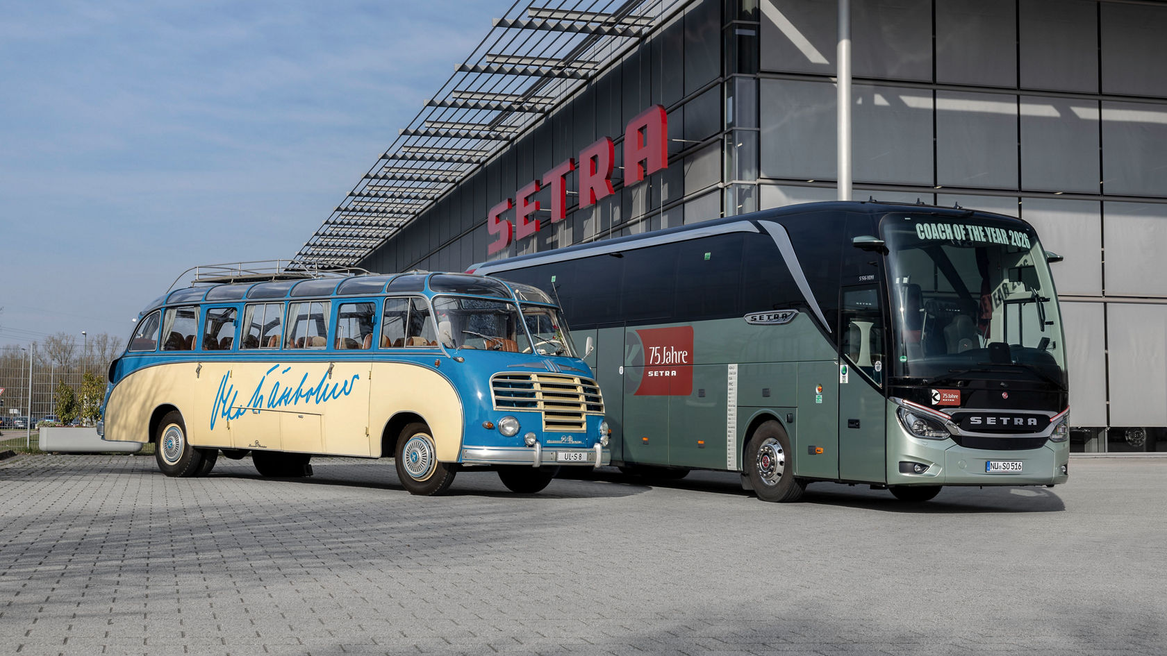 Modern green-grey Setra TopClass touring coach standing next to a historic Setra classic bus, in the background a section of the glass facade of the Setra Customer Centre in Neu-Ulm.