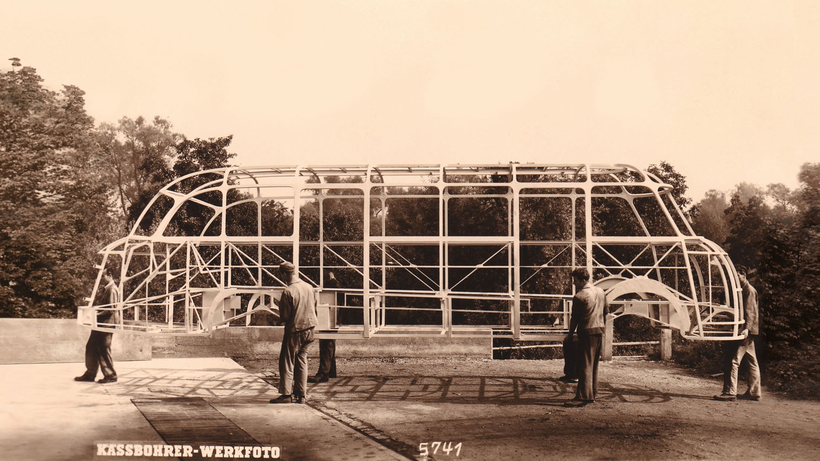 Historic plant photo: workers carrying the body frame of a bus outdoors, side view