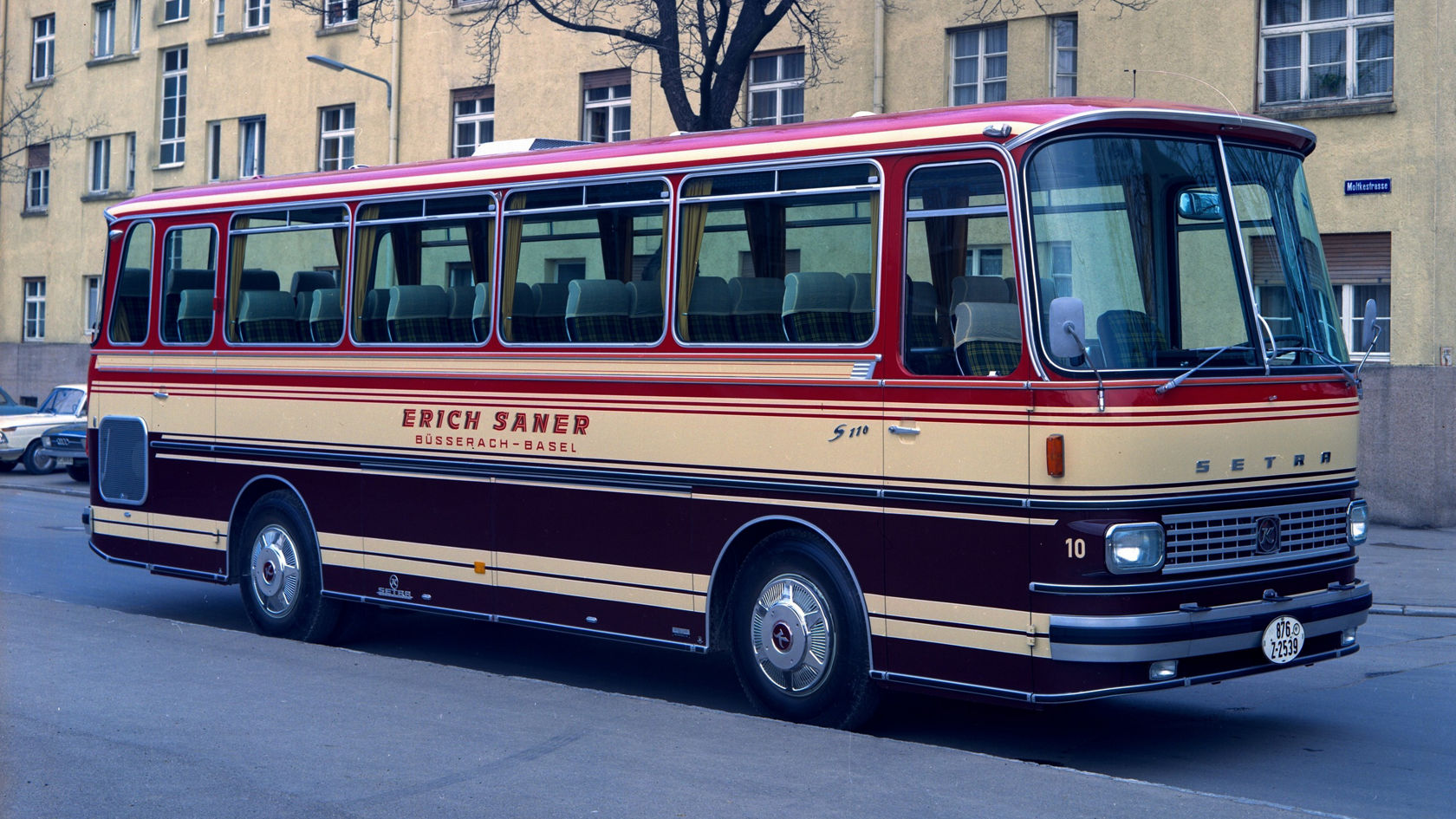 Historic Setra S 110 touring coach in red and beige, side view parked on a city street in front of a residential building