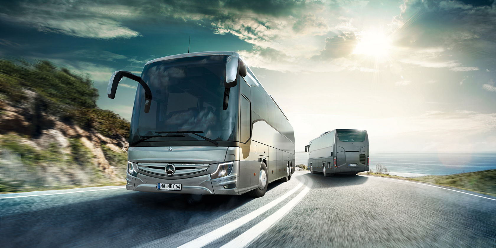 Zwei Mercedes-Benz Tourismo Reisebusse auf einer Küstenstraße, ein Bus im Vordergrund, sonniger Himmel im Hintergrund