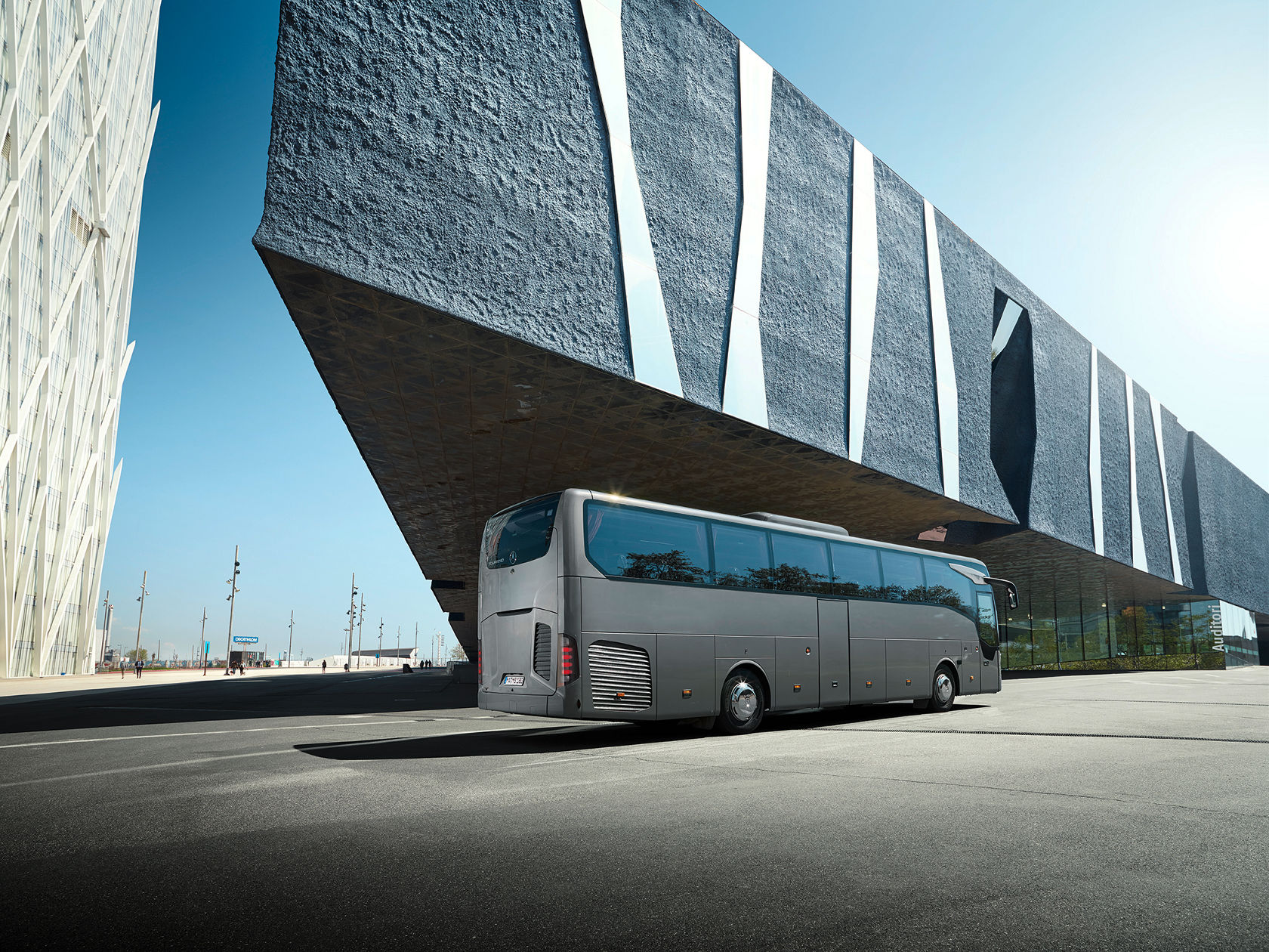 Mercedes-Benz Tourismo Reisebus vor moderner Architektur mit Glasfassade auf urbanem Platz