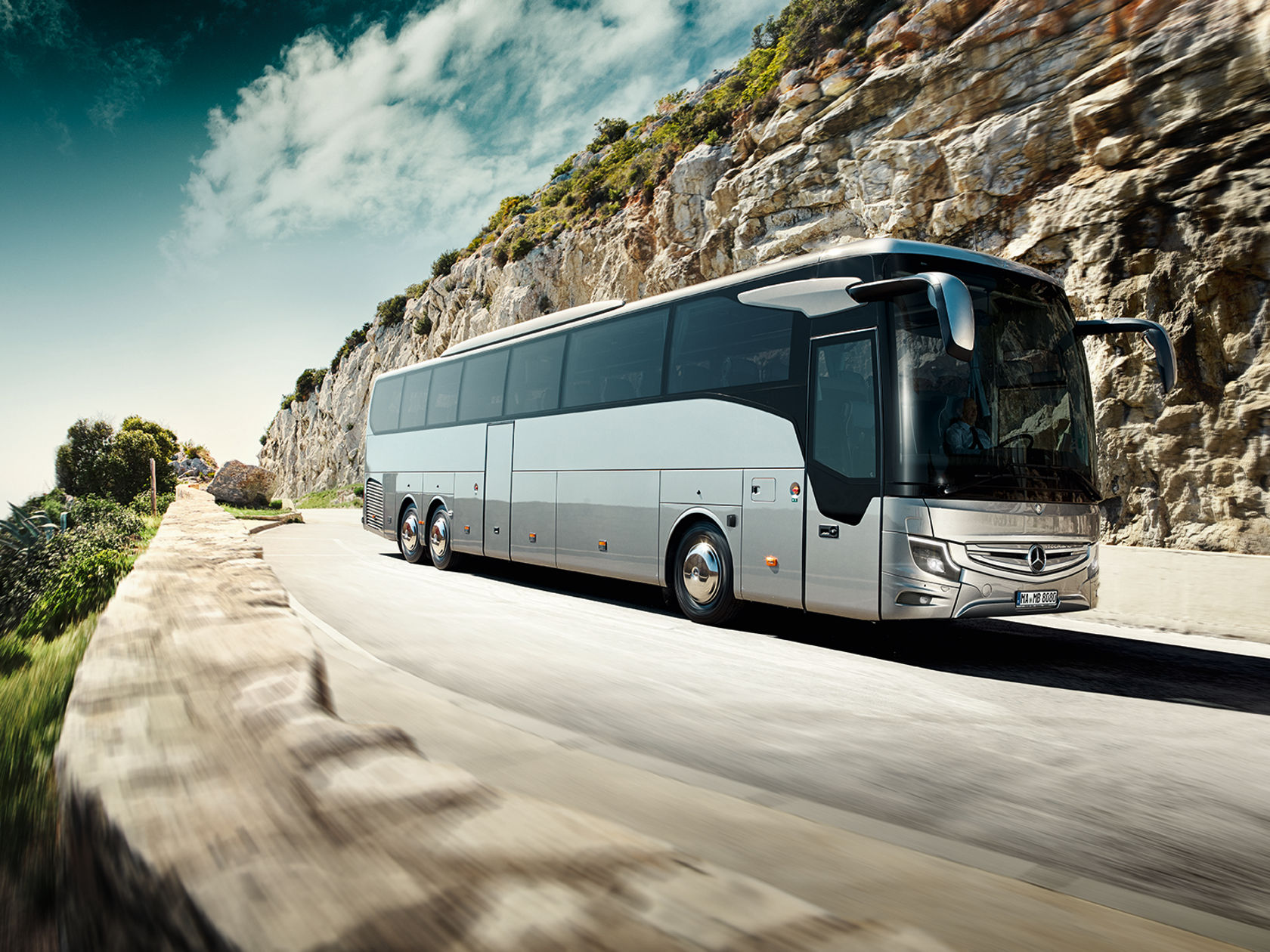 Mercedes-Benz Tourismo L Reisebus fährt auf Küstenstraße entlang einer Felswand, mit Meerblick und blauem Himmel