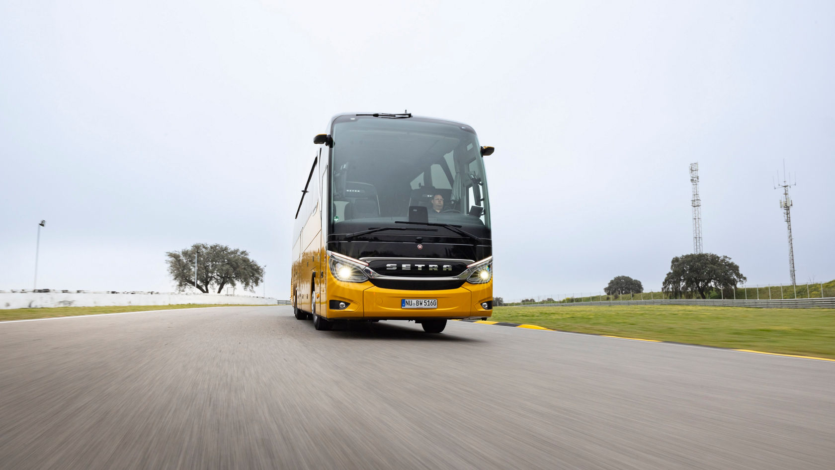 Autobus da turismo Setra TopClass in marcia sul circuito di prova, vista frontale con luci accese su un'ampia curva asfaltata