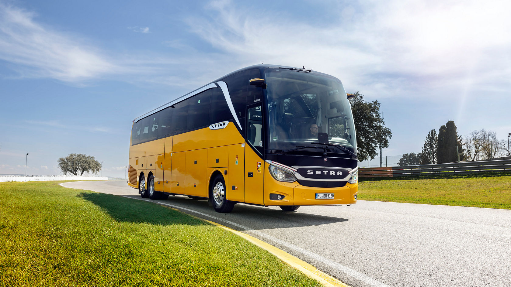 Gul Setra TopClass turistbuss kör på en teststräcka i dagsljus, sedd framifrån med Setra-logotyp