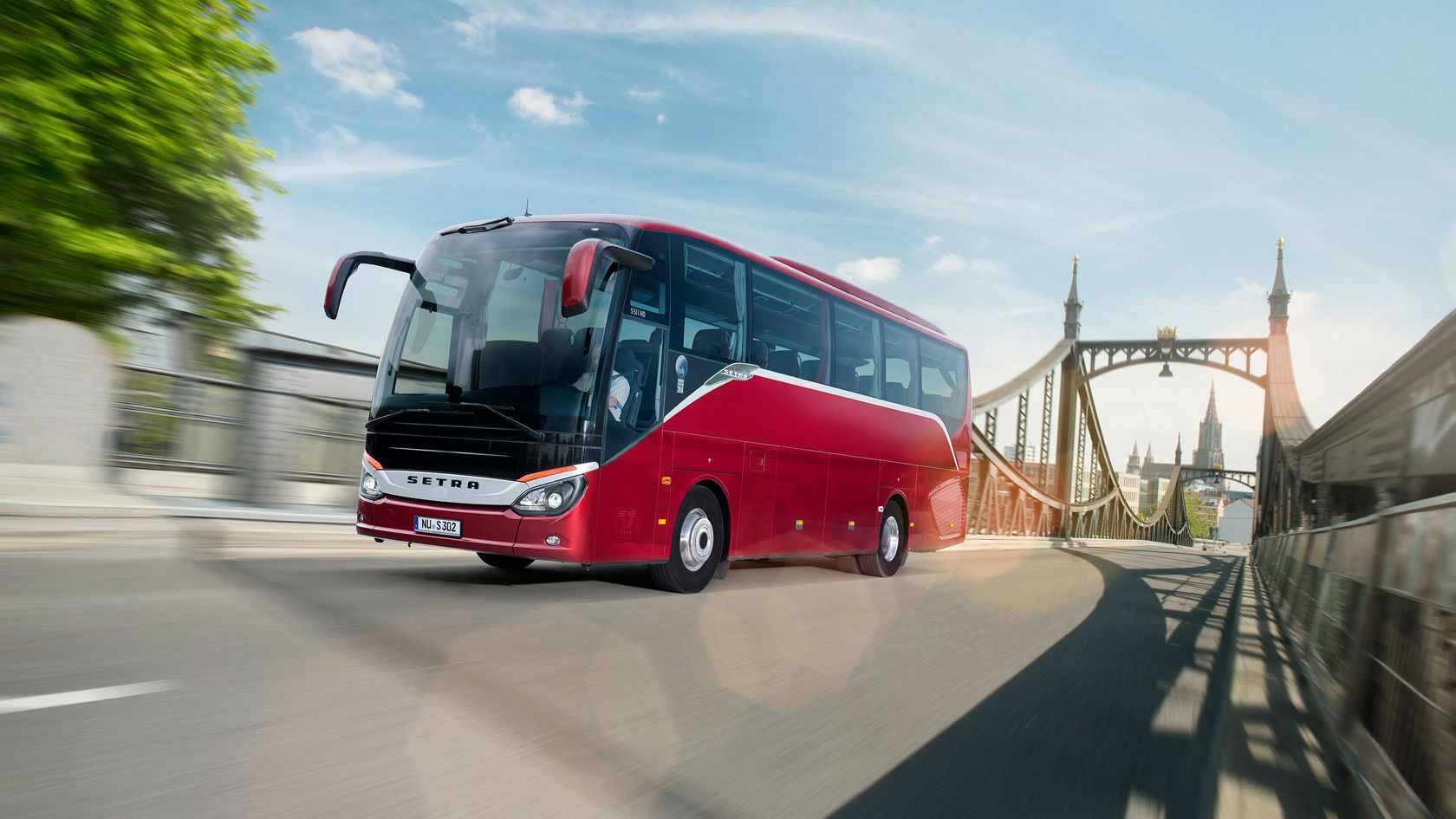 Red Setra ComfortClass touring coach driving over a bridge in the city, front view at an angle from the left in daylight