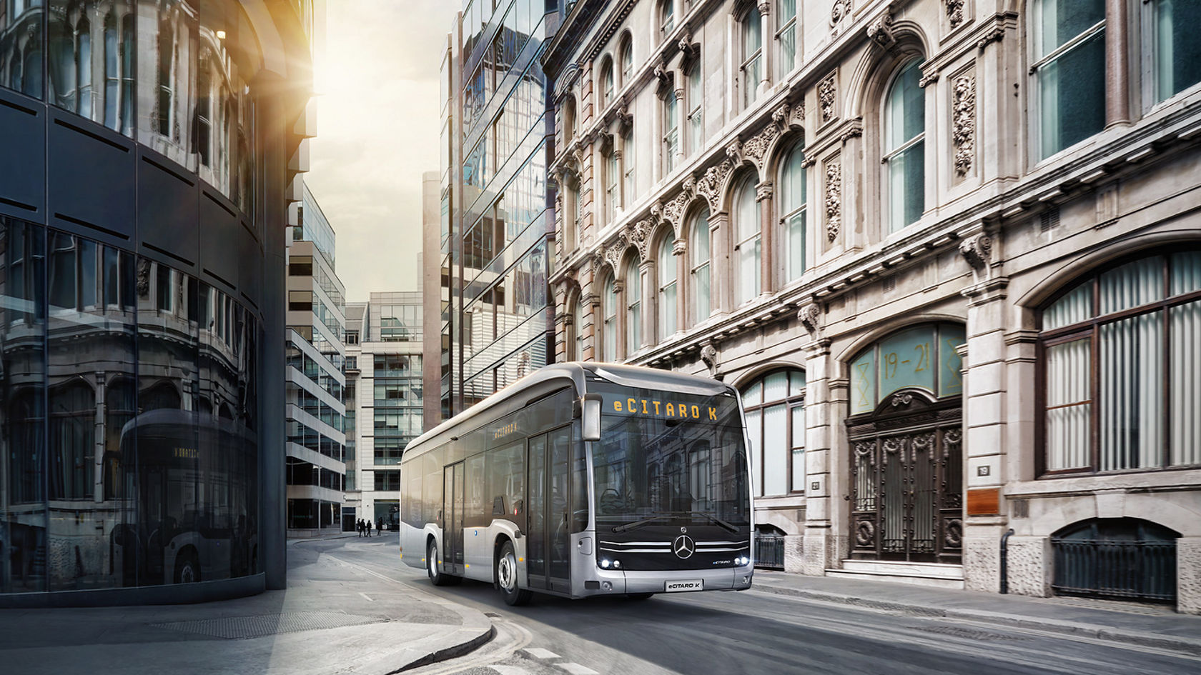 Mercedes-Benz eCitaro city bus driving through inner-city street, surrounded by glass facades and old buildings