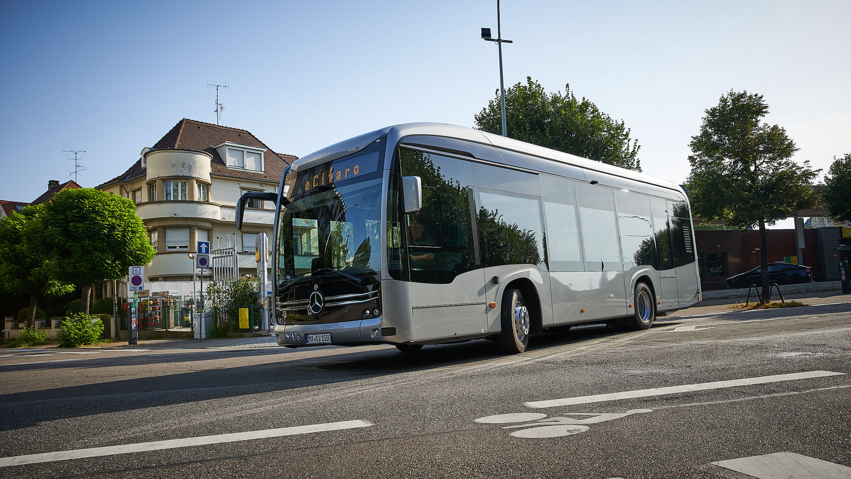 Mercedes-Benz eCitaro Stadtbus fährt durch ein Wohngebiet, Seitenansicht an einer Kreuzung