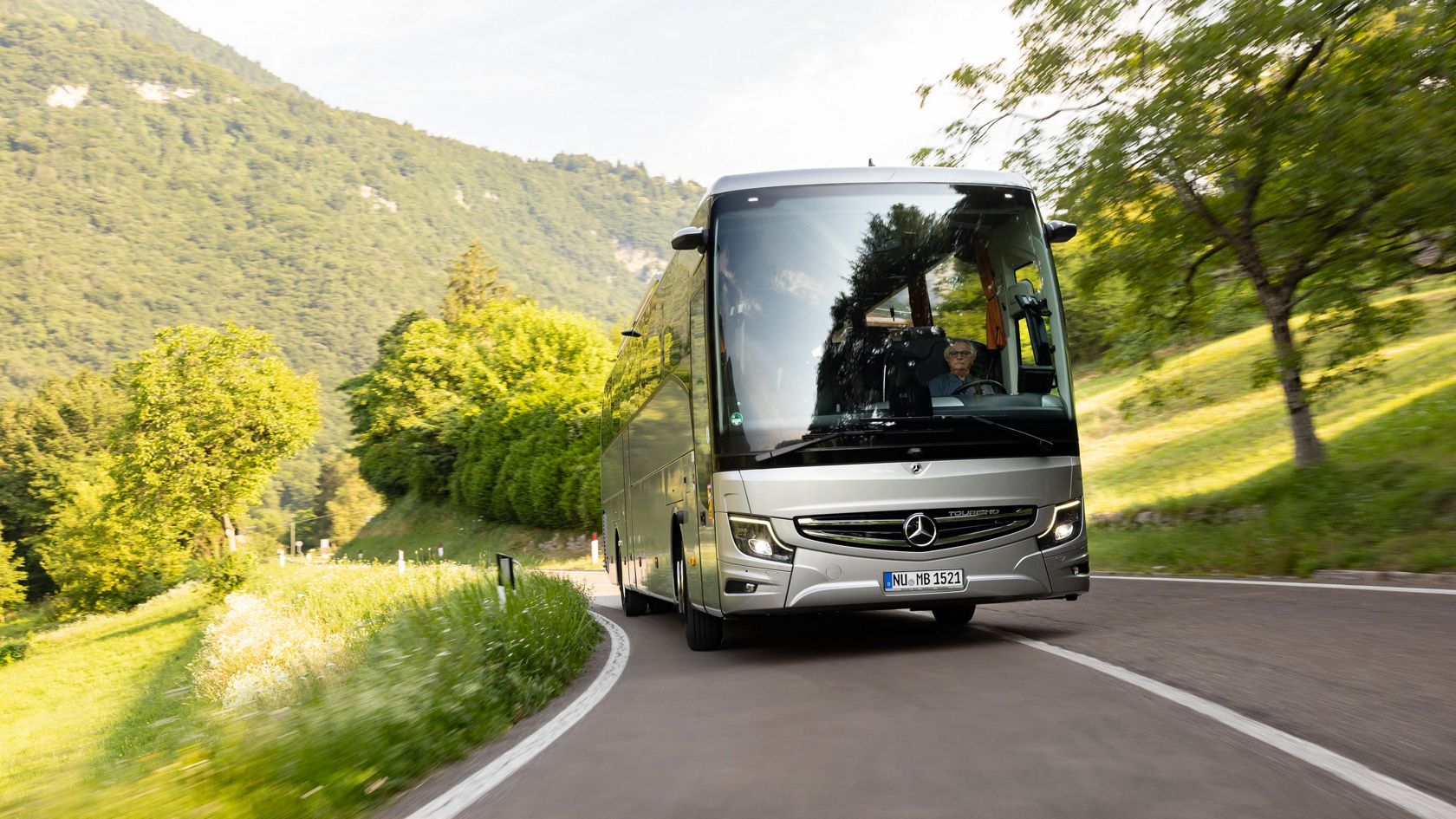Mercedes-Benz Tourismo Reisebus fährt auf einer kurvigen Landstraße durch eine grüne Berglandschaft