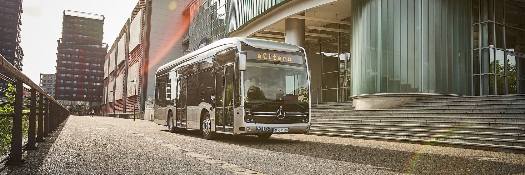 Mercedes-Benz eCitaro Stadtbus vor modernem Glasgebäude in der Stadt