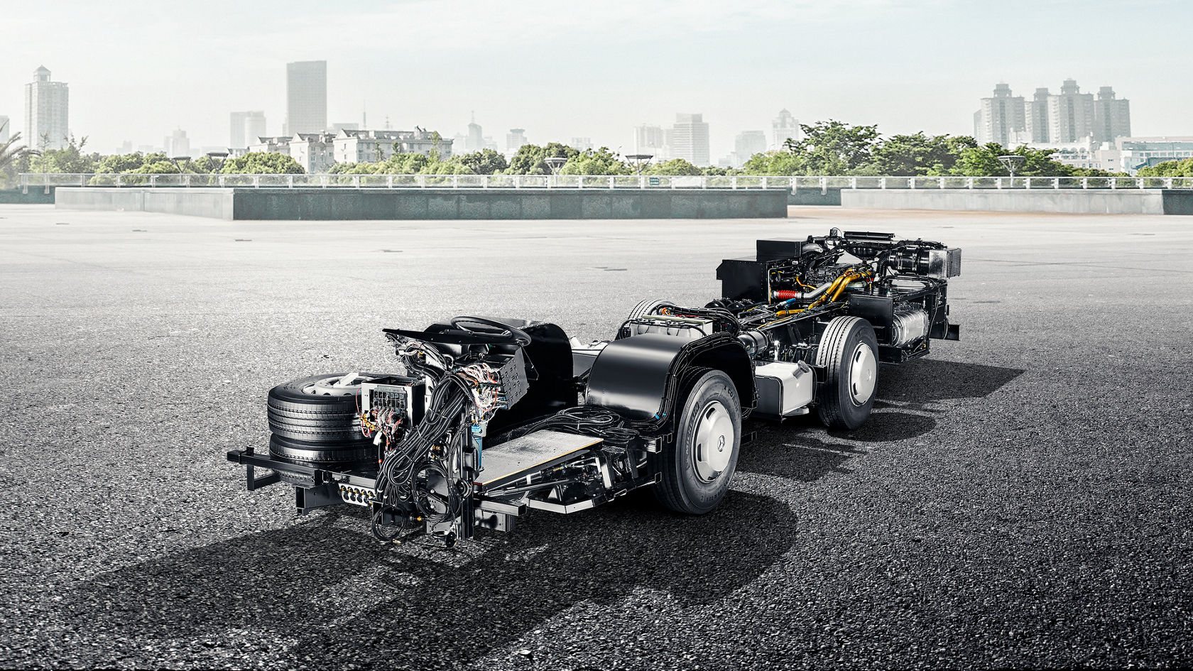 Mercedes-Benz OC 500 LE bus chassis on an open test area, with a city skyline in the background