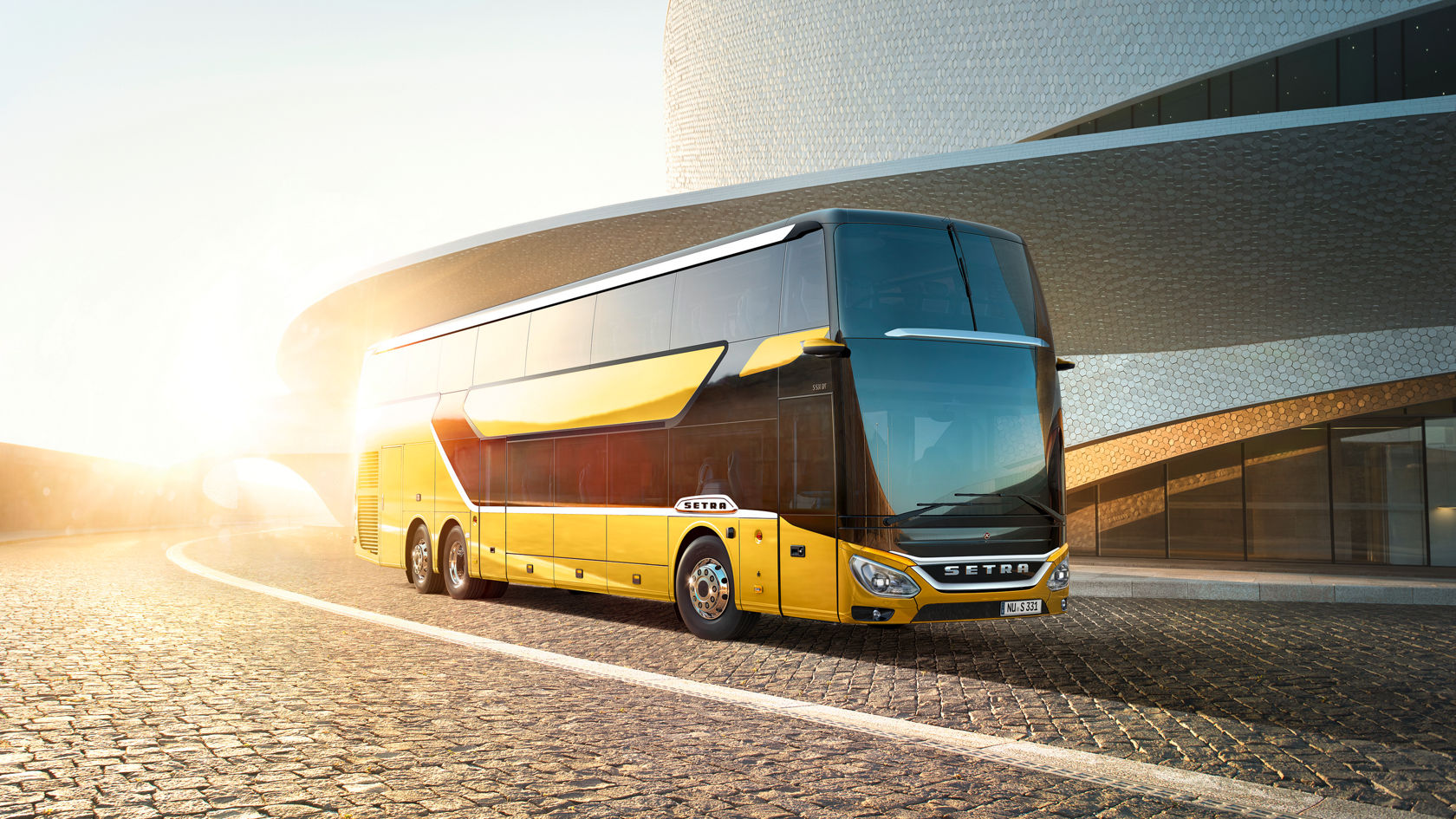 Setra Doppelstock-Reisebus in gelb-gold steht vor moderner Architektur bei tief stehender Sonne