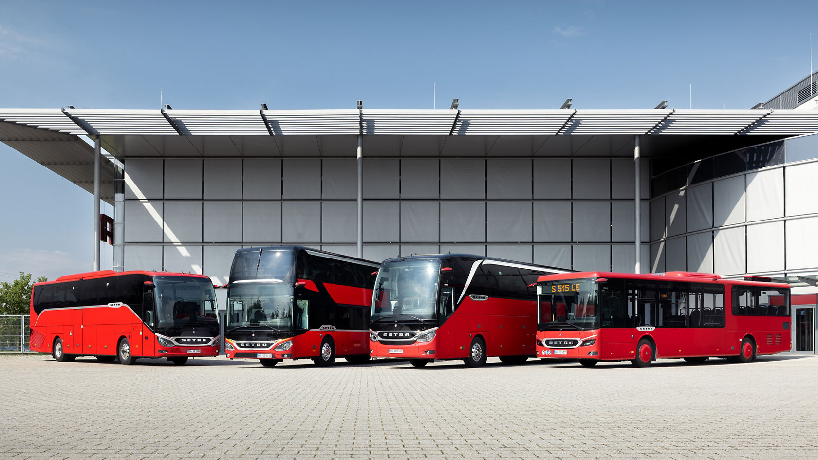 Four different red Setra bus models in front of a modern company building: Setra ComfortClass touring coach, Setra double-decker, Setra TopClass touring coach and Setra MultiClass side by side