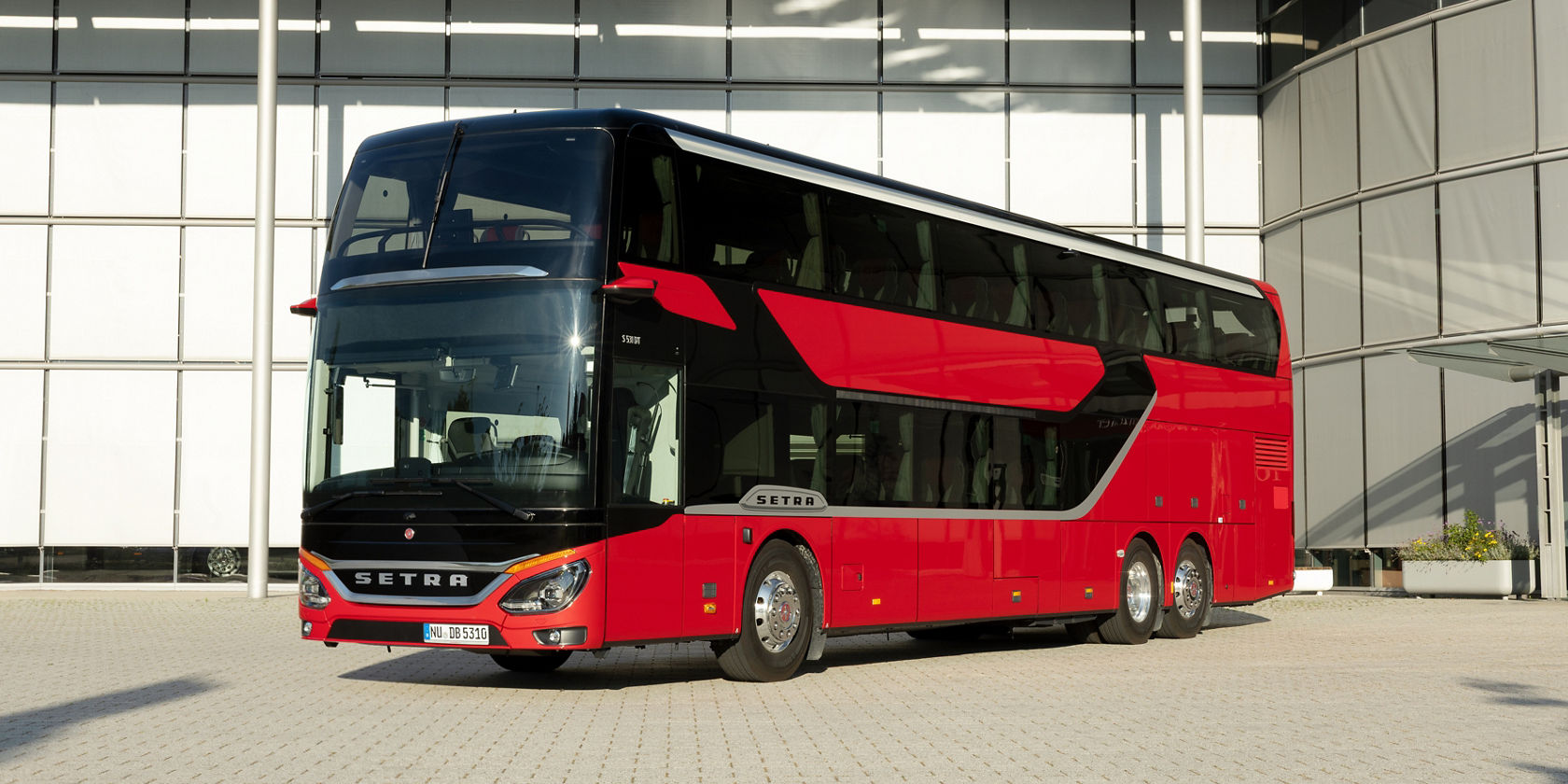 Roter Setra S 531 Doppelstock-Reisebus steht vor auf dem Setra Werksgelände vor dem Kundencenter mit moderner Glasfassade, Dreiviertelansicht von vorn