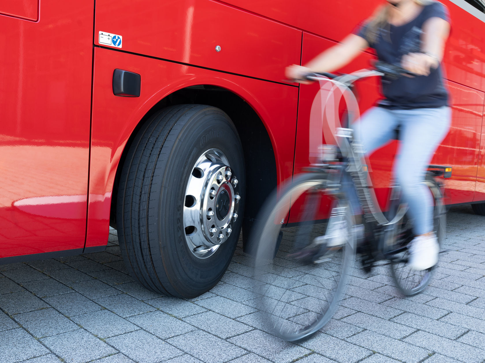 Rueda delantera de un autocar Setra rojo con llanta visible, mientras una ciclista pasa desenfocada junto al vehículo