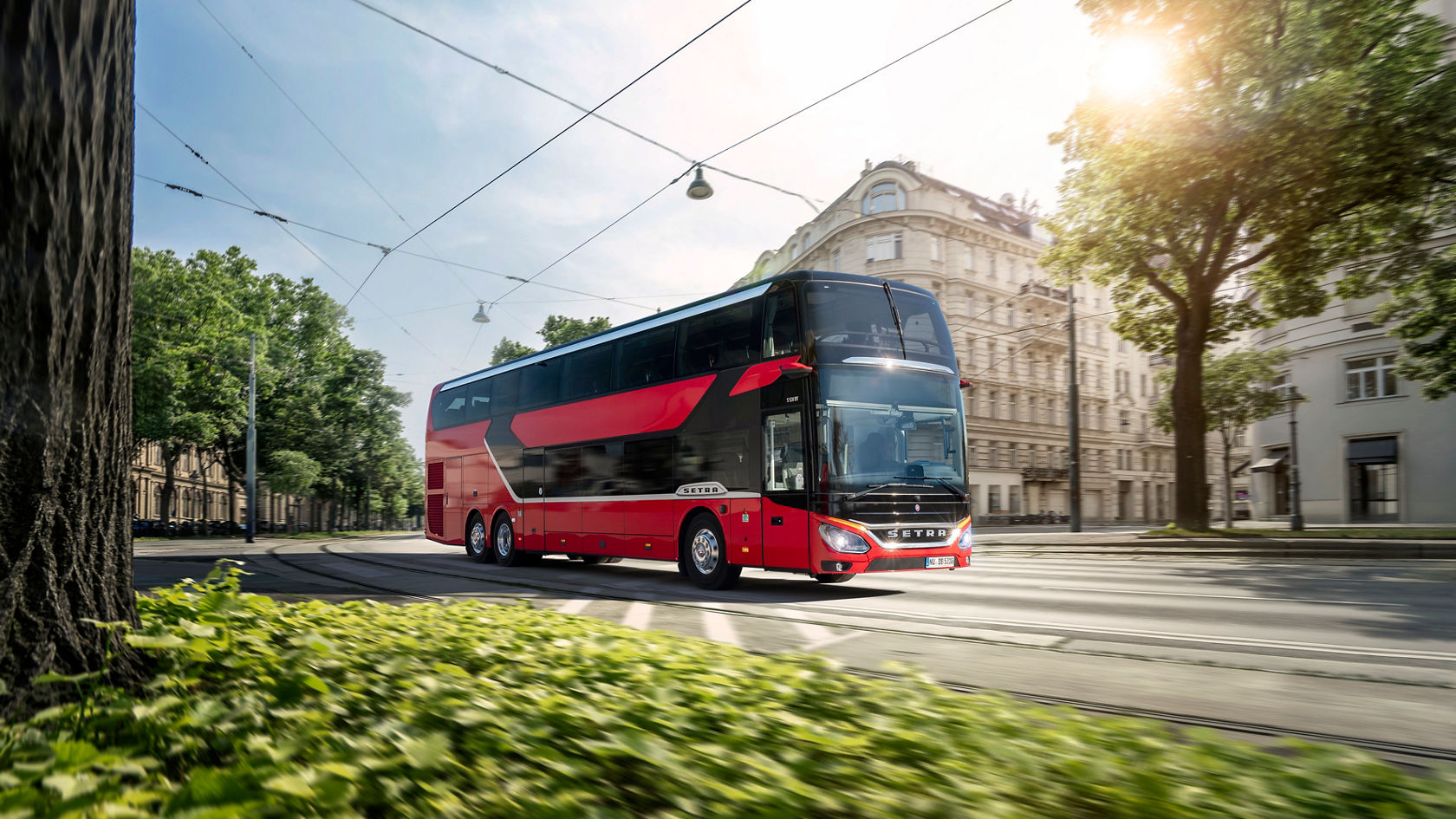 Roter Setra Doppelstock-Reisebus fährt durch eine Stadtstraße mit Oberleitungen, Bäumen und historischen Gebäuden