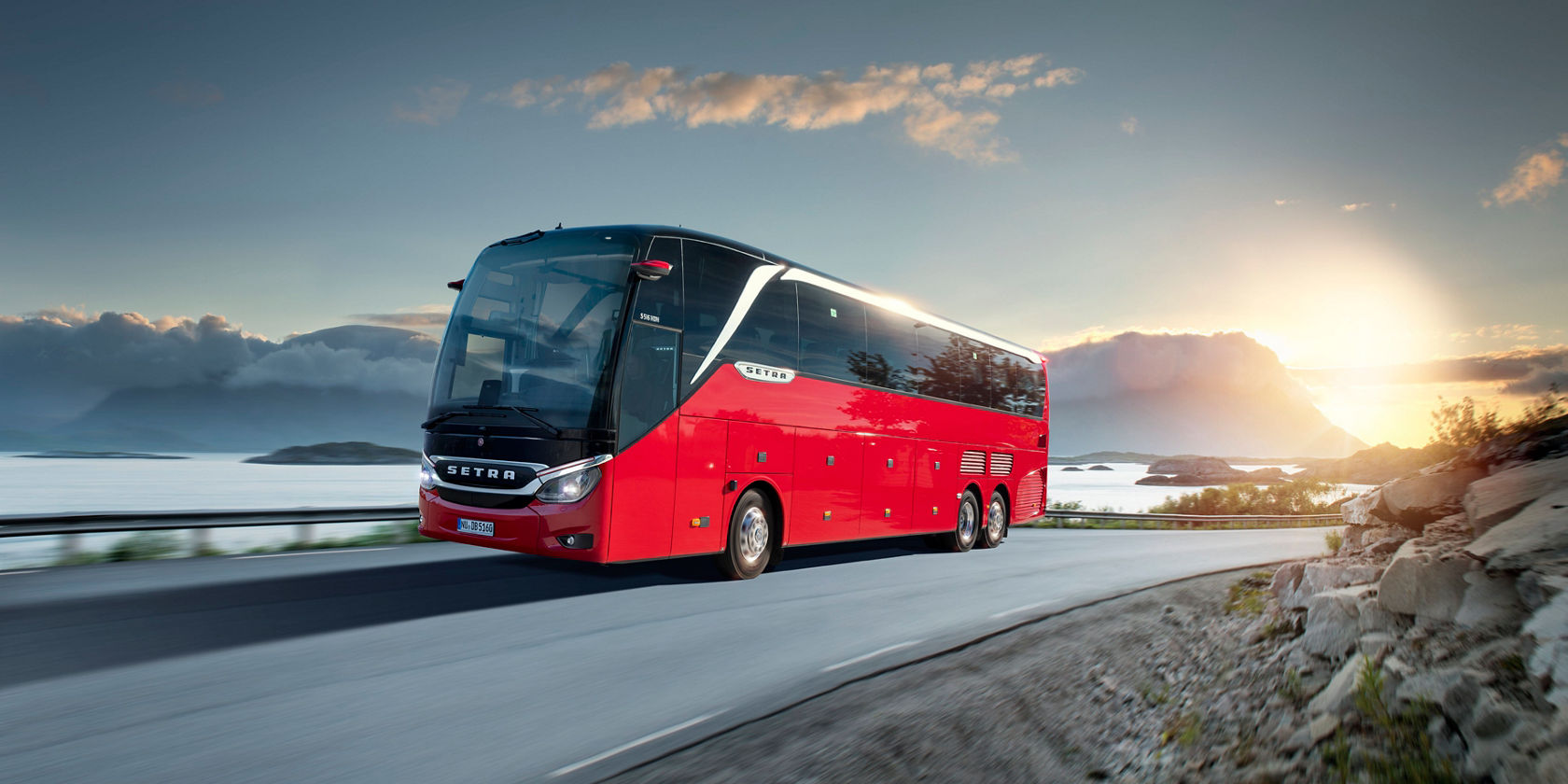 L'autobus da turismo rosso Setra TopClass viaggia al tramonto su una strada costiera davanti al mare e al panorama delle nuvole