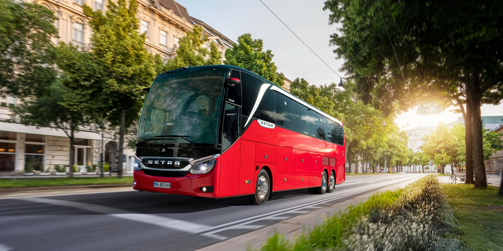 L'autobus da turismo Setra TopClass attraversa una strada urbana alberata, l'autobus da turismo rosso davanti a edifici storici alla luce della sera
