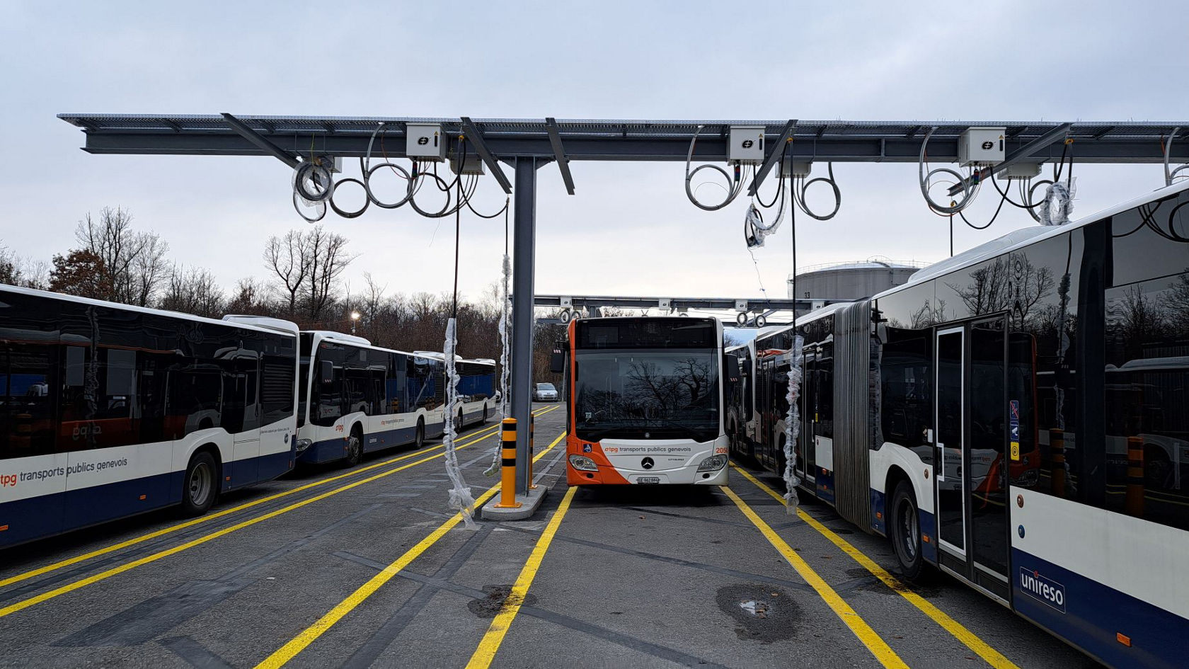 Mercedes‑Benz Elektro‑ und Stadtbusse stehen unter einer Ladeinfrastruktur auf einem Betriebshof; ein orange‑weißer Mercedes-Benz Bus der TPG positioniert sich zentral unter dem Pantograph‑Ladesystem.