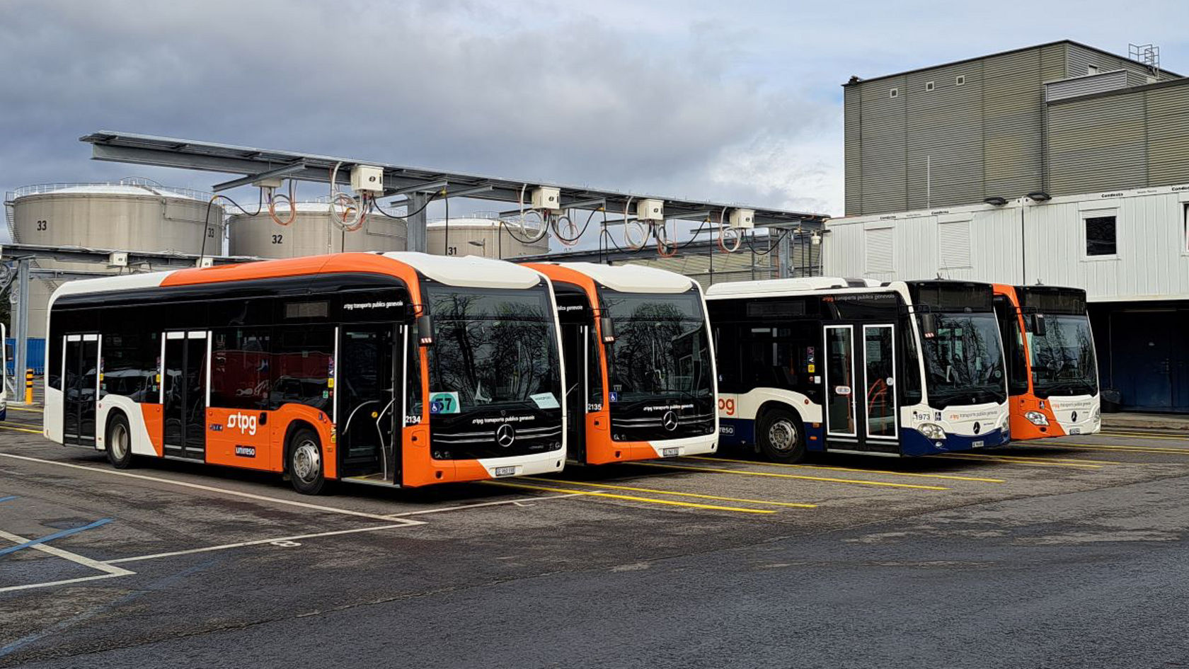 Mercedes‑Benz city buses at a depot in front of industrial plants; modern electric and city bus models from DTPG in use for local public transport.