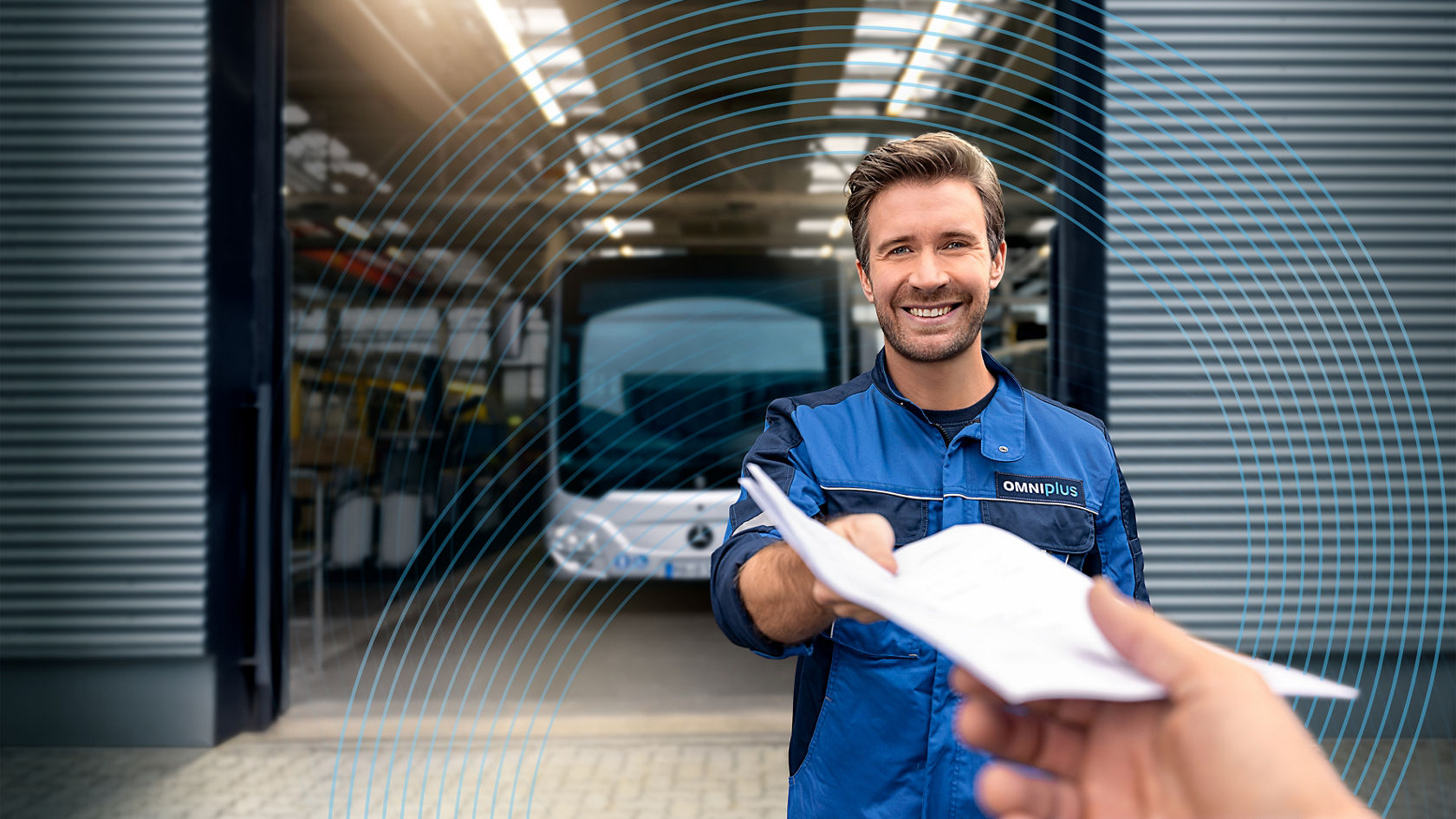 Huoltotyöntekijä OMNIplus-työasussa luovuttaa asiakirjoja korjaamon edessä, taustalla on Mercedes-Benz-kaupunkiliikennebussi tehdashallissa. 