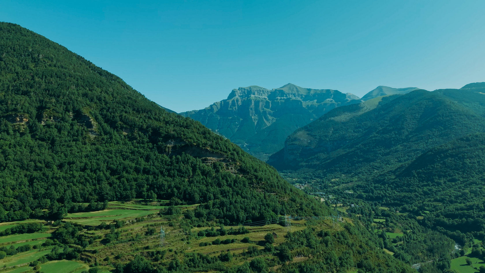 Weite Berglandschaft mit bewaldeten Hängen und Tal entlang einer Überlandroute.