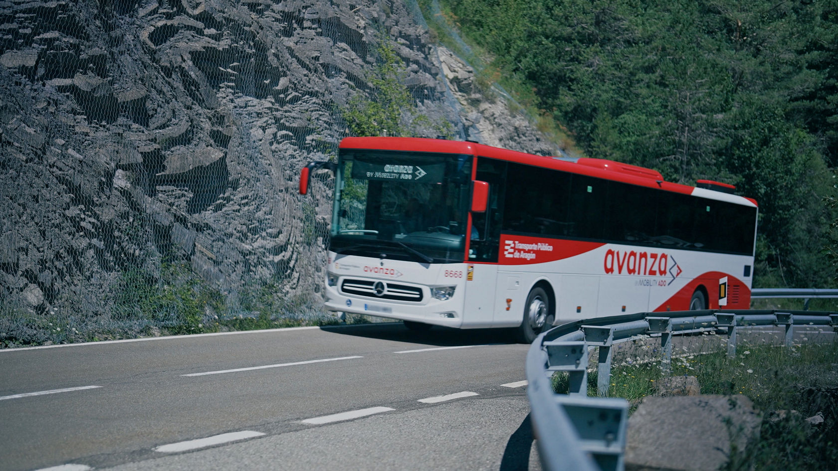 Mercedes-Benz Überlandbus Intouro fährt auf einer schmalen Bergstraße entlang einer Felswand im Überlandverkehr.