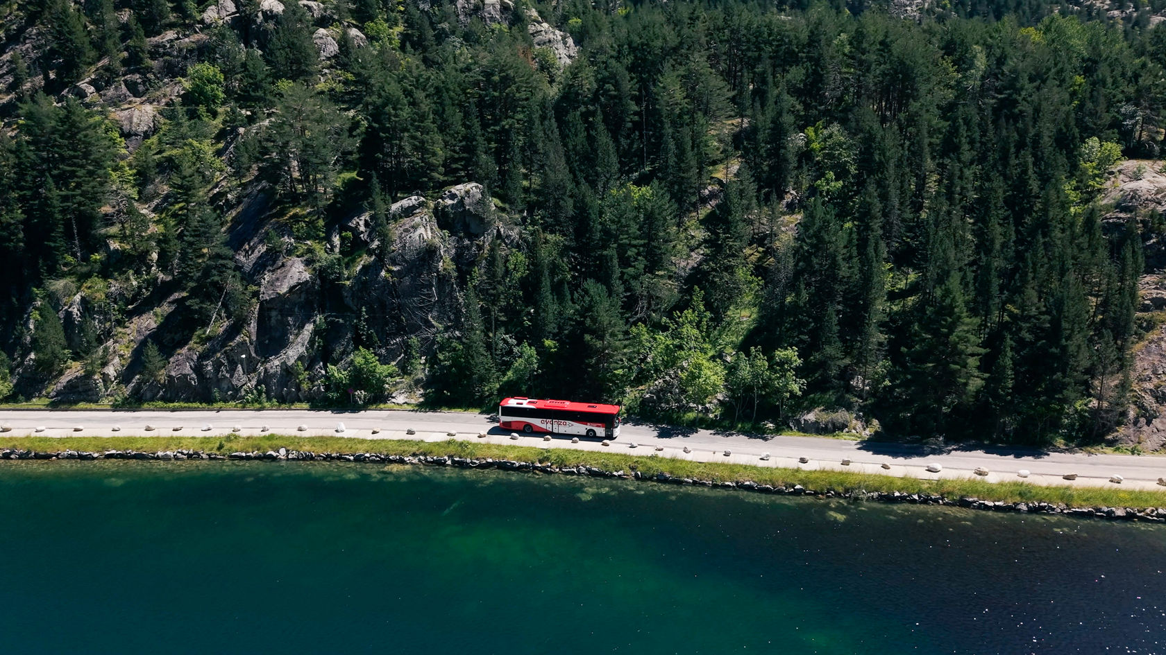 Mercedes-Benz Überlandbus Intouro auf einer Bergstraße entlang eines Bergsees in bewaldeter Berglandschaft. 