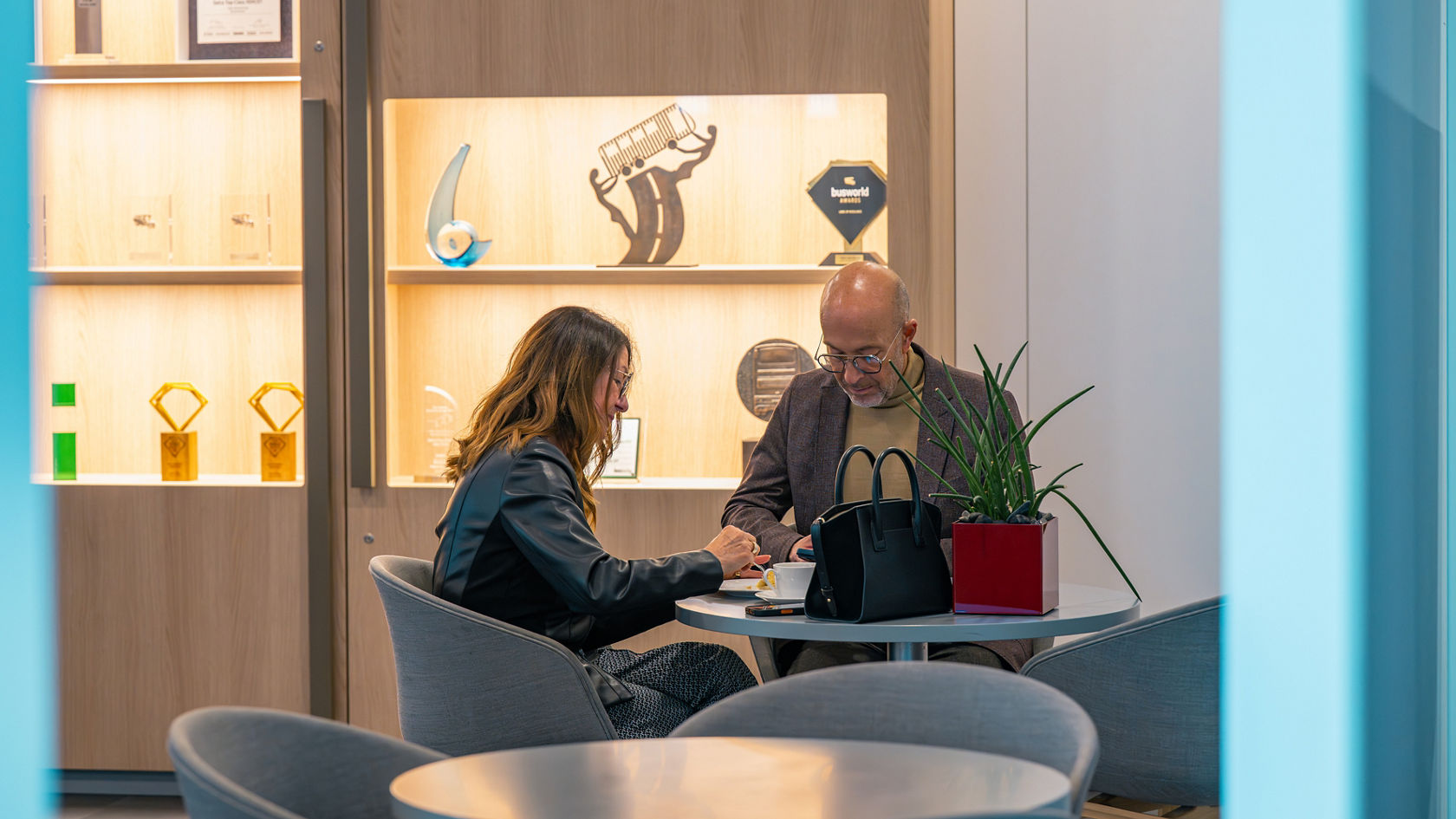 Due persone siedono a un tavolo nel Centro Clienti Setra davanti a una parete di presentazione illuminata con premi.