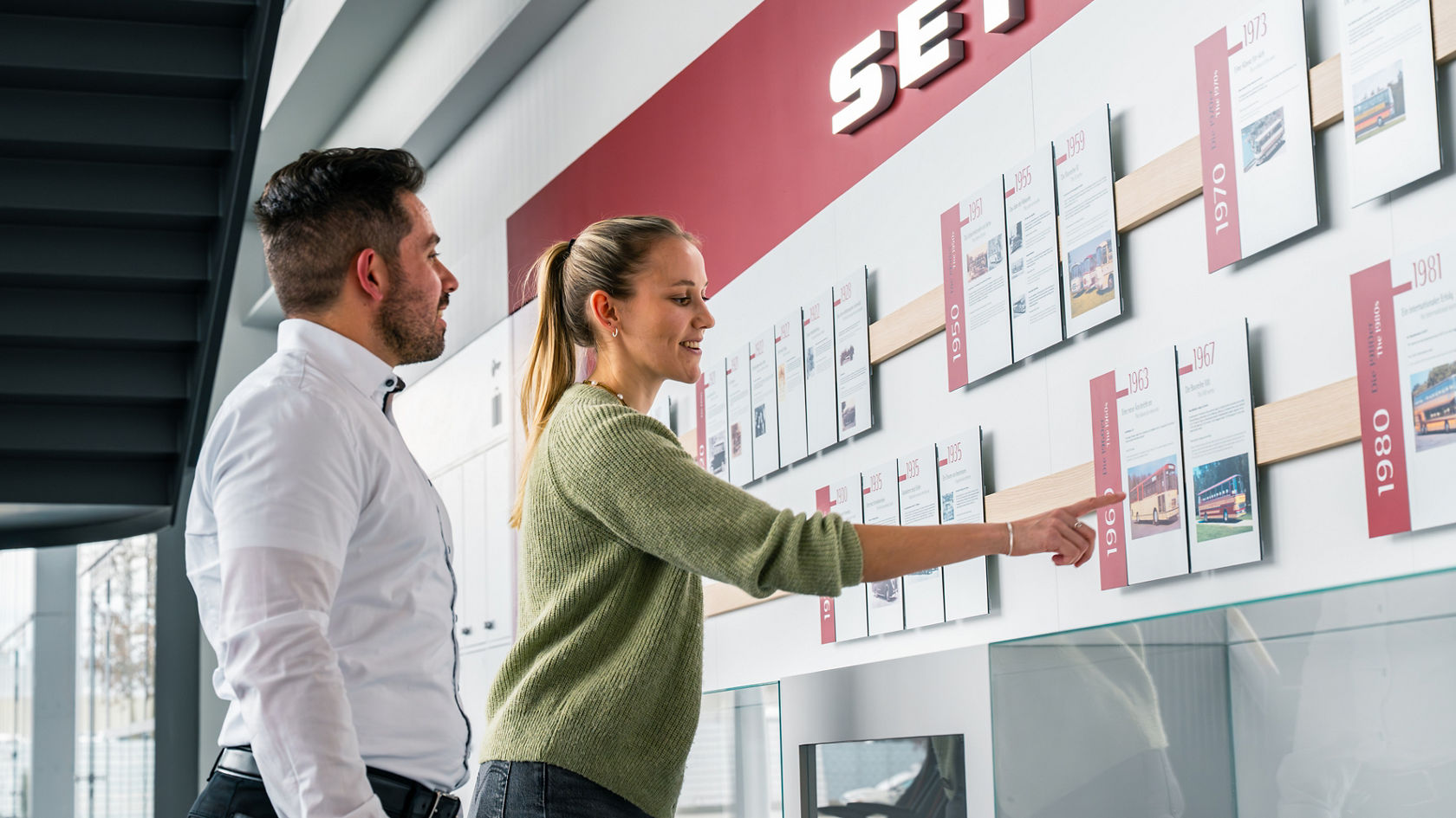 Due persone osservano la parete della cronologia Setra con documenti storici ed oggetti esposti nel Centro Clienti.