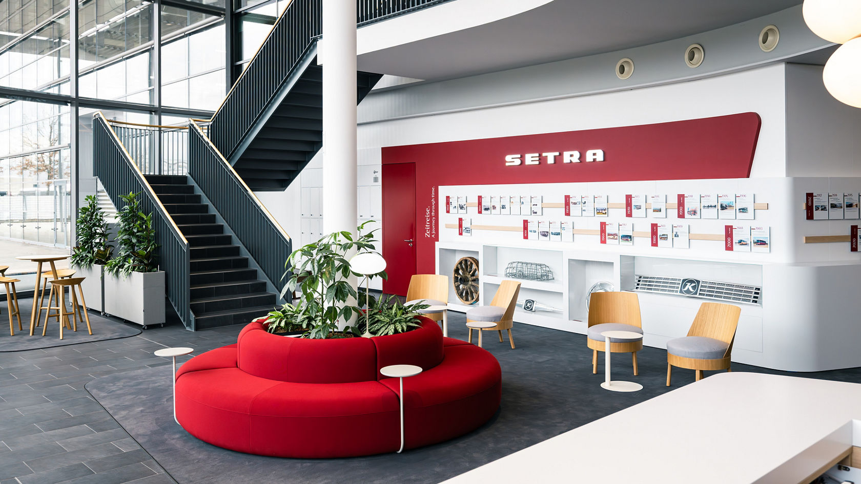 Interno del Centro Clienti Setra con scale aperte, numerose postazioni a sedere e incisiva parete del marchio e della storia Setra.