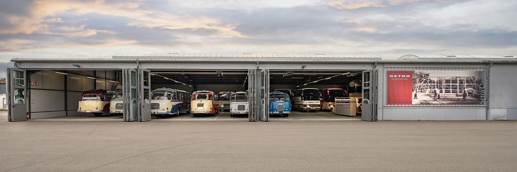 Kässbohrer Halle met geopende deuren en meerdere historische Setra bussen, tentoongesteld in een rij voertuigen