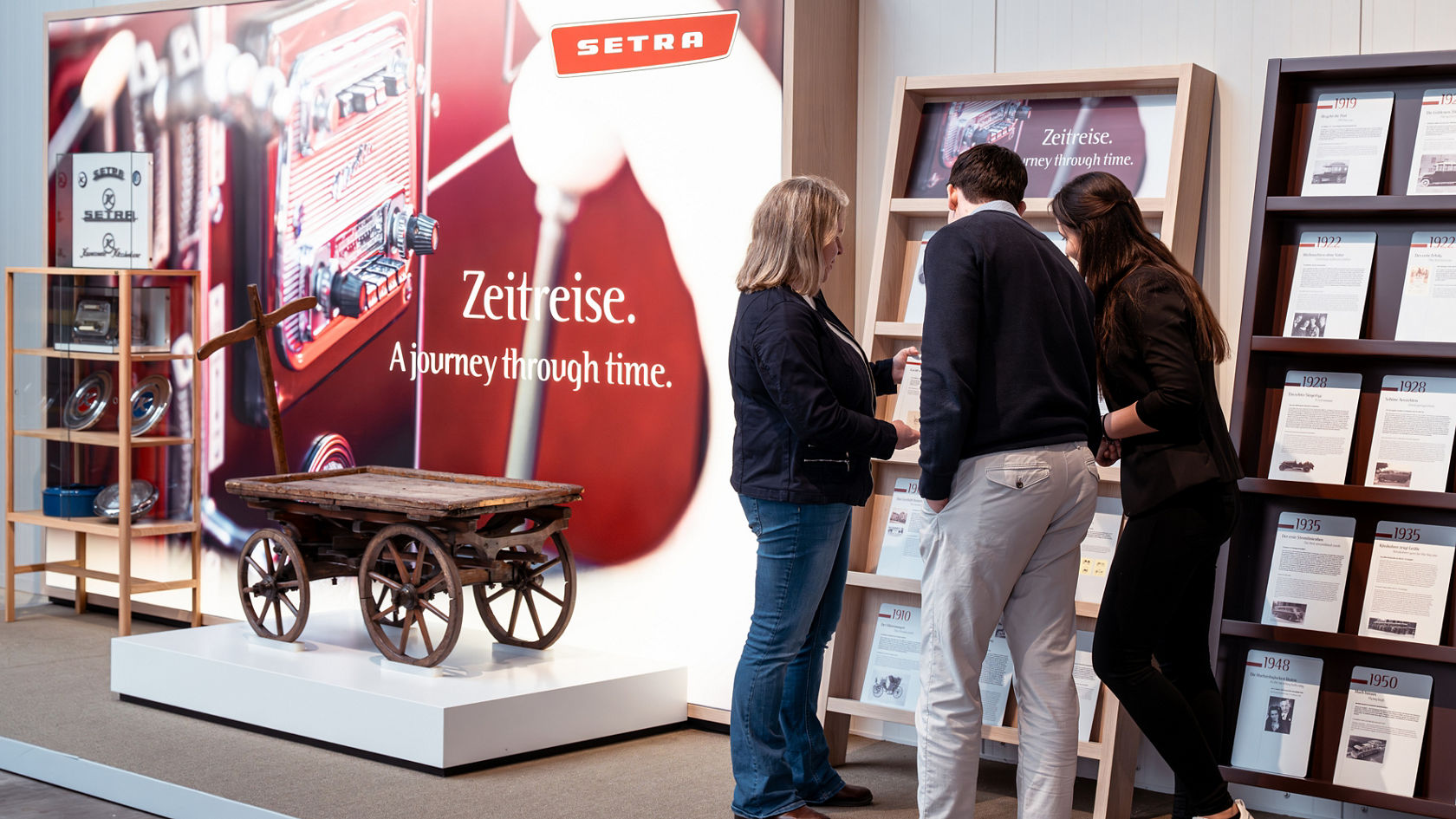 Bezoekers lezen in de Kässbohrer-hal een tijdlijn over de geschiedenis van Setra, naast de tentoonstellingswand 'Tijdreis'
