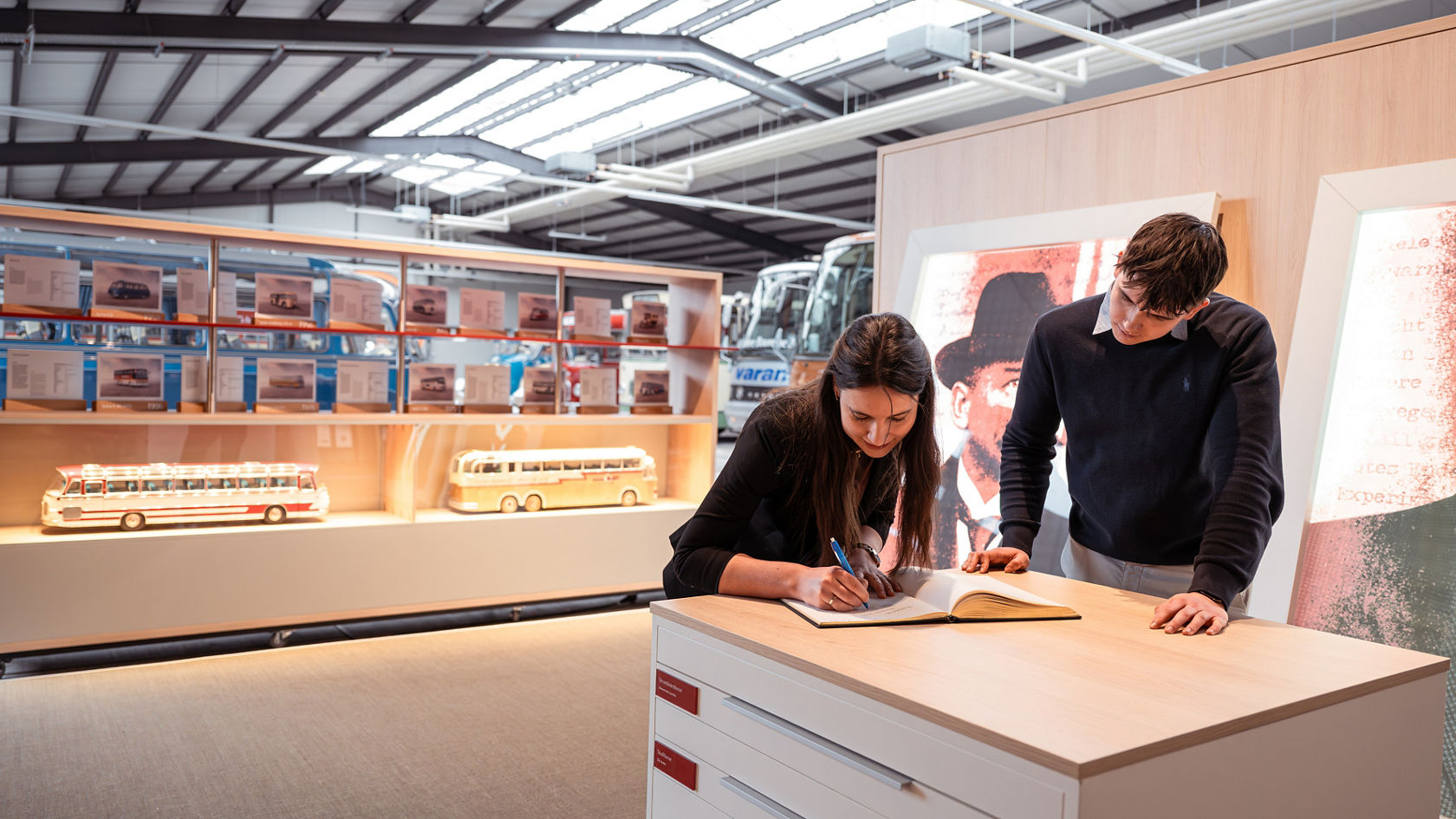Bezoekers schrijven zich in de Kässbohrer-hal in een gastenboek in, op de achtergrond Setra busmodellen in vitrines