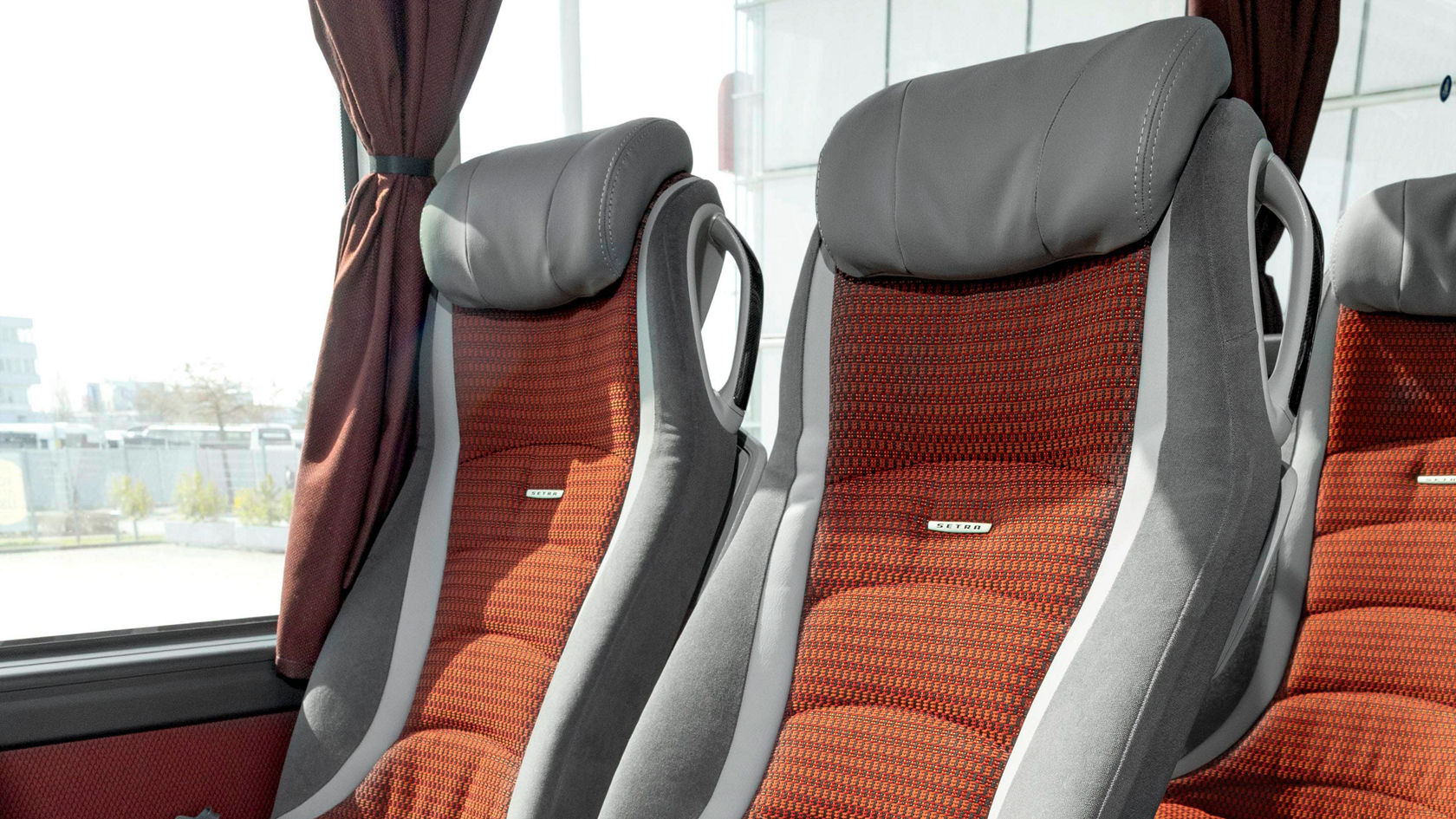 Abitacolo dell'autobus da turismo Setra TopClass con sedili in fila, vista su due file di sedili con sedili rosso-grigi e emblema Setra