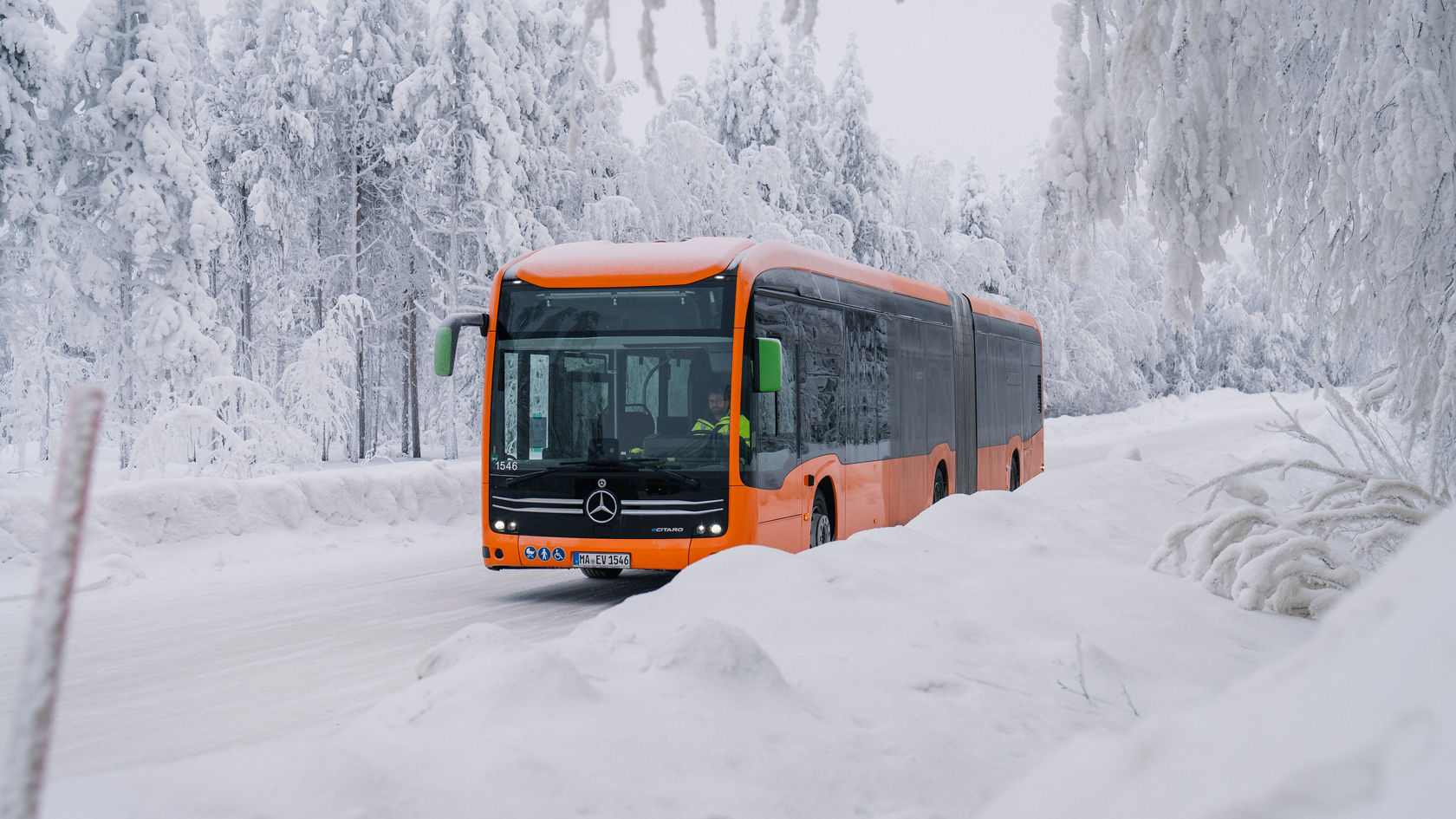 Pomarańczowy autobus przegubowy Mercedes-Benz eCitaro jedzie po ośnieżonej drodze przez zimowy las