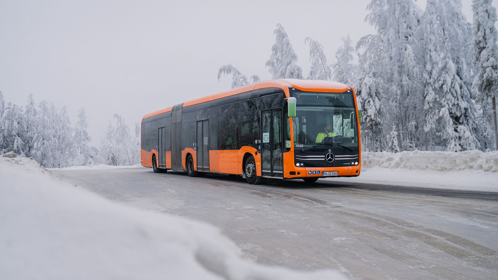Autobus articulé Mercedes-Benz eCitaro orange roulant sur une route hivernale verglacée, arbres enneigés en arrière-plan, vue latérale du bus