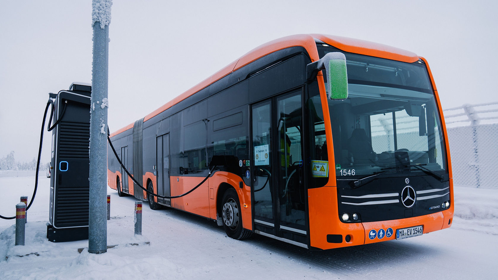 Autobus articulé Mercedes-Benz eCitaro à une borne de recharge en hiver, avec câble de charge branché sur un terrain enneigé