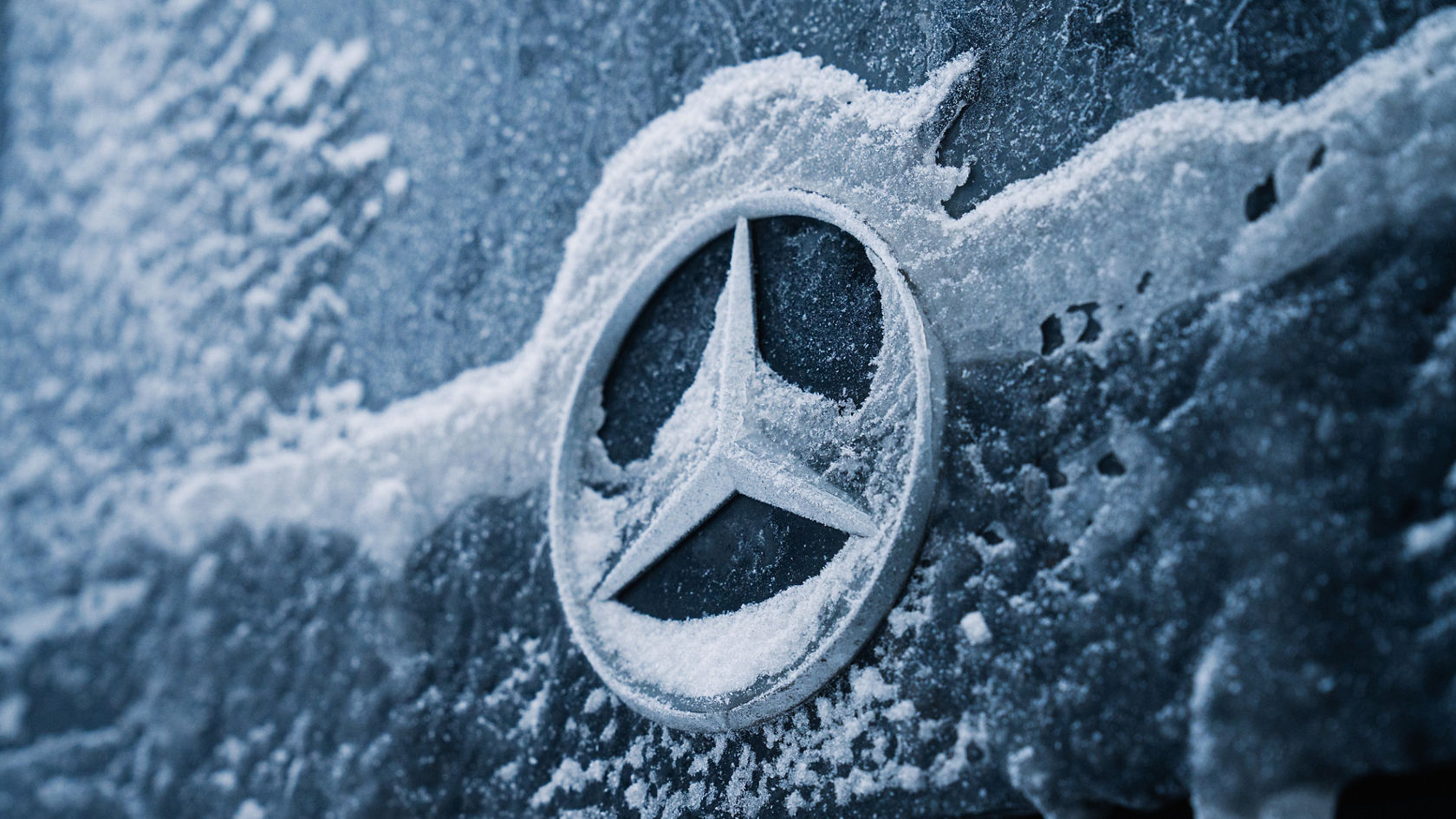 Gros plan sur l’étoile Mercedes-Benz givrée sur la carrosserie, avec de la neige et des cristaux de givre