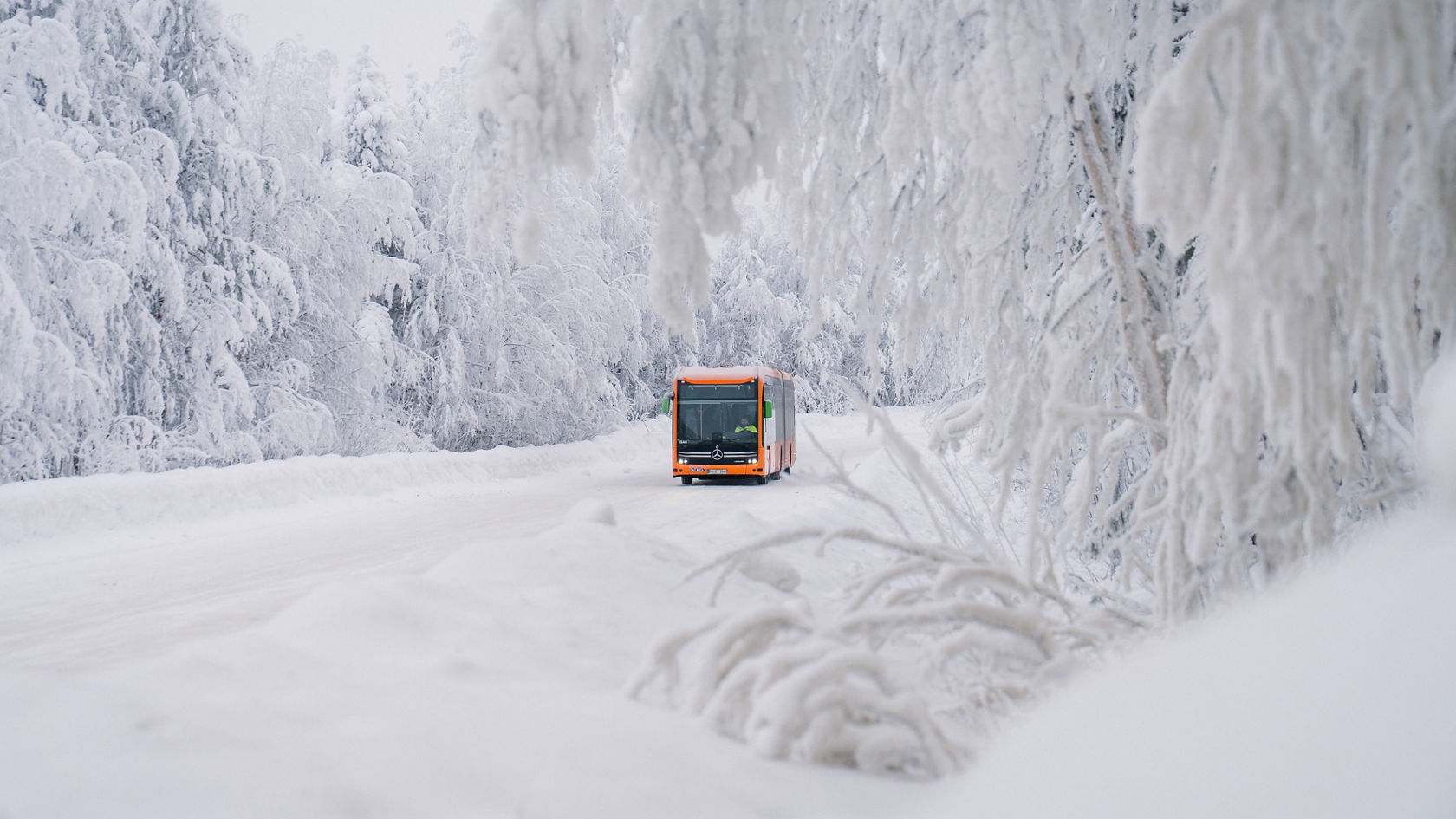 Un Mercedes-Benz eCitaro roule sur une route enneigée à travers une forêt hivernale avec des arbres givrés