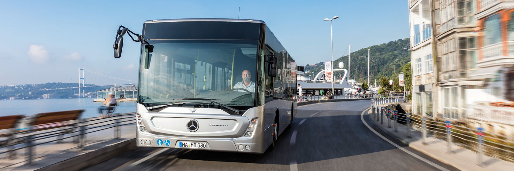 Gradski autobus Mercedes-Benz Conecto vozi na putu duž urbanog obalnog landšafta