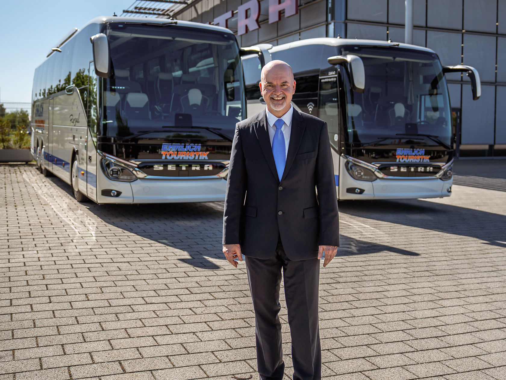 Hombre con traje delante de dos autocares Setra en la plaza del centro de atención al cliente de Setra en Neu-Ulm con el cielo azul