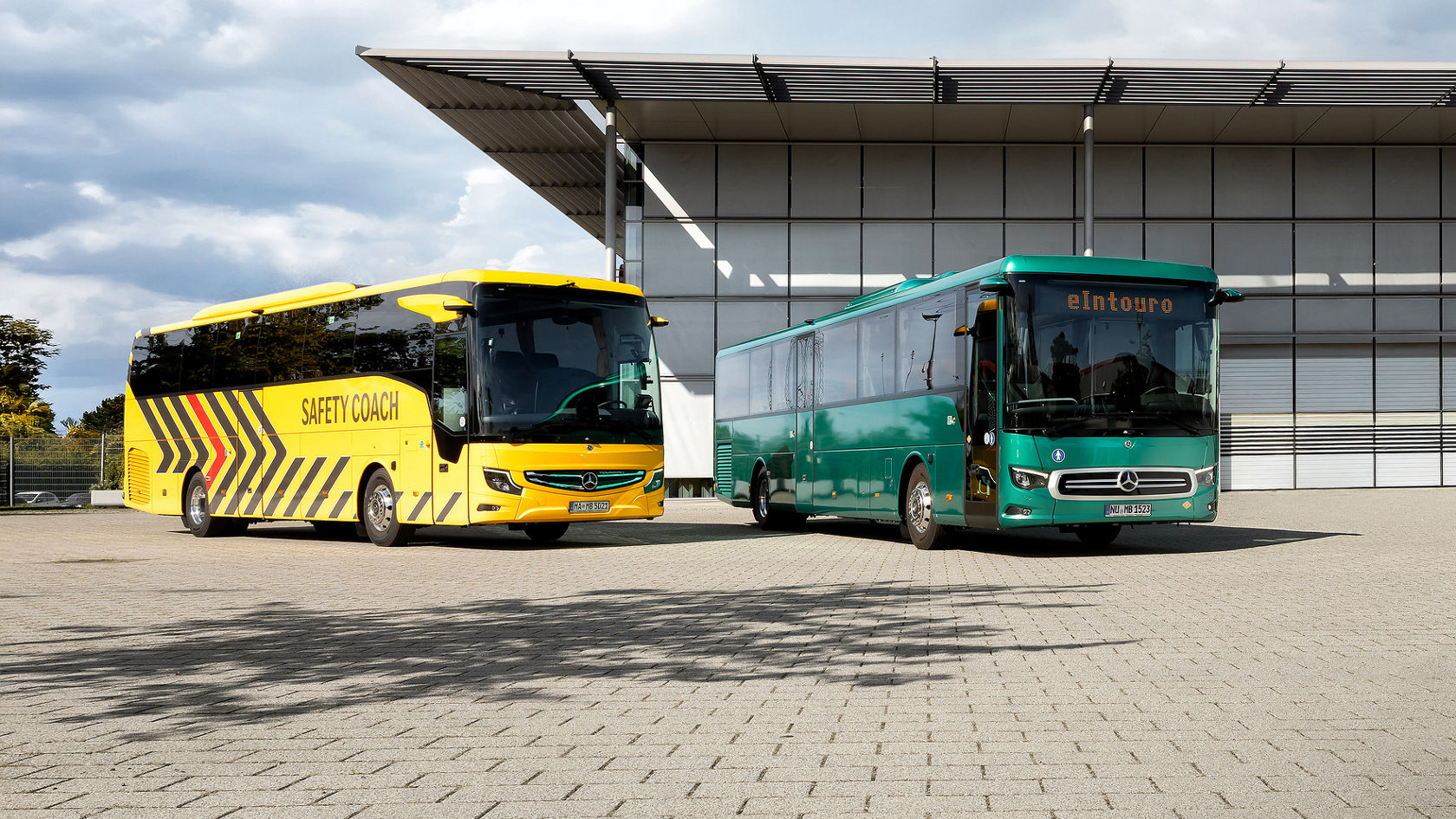 Mercedes-Benz eIntouro e Safety Coach davanti a un moderno capannone su un terreno pavimentato sotto un cielo nuvoloso
