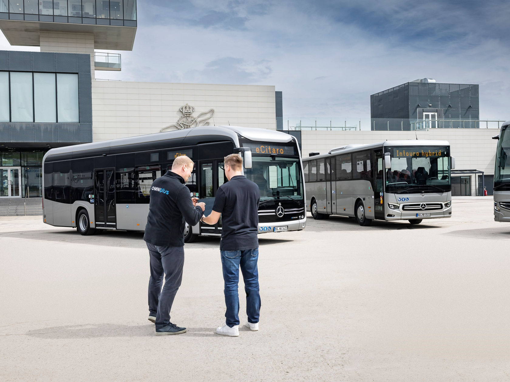 Dwóch pracowników serwisu OMNIplus przed dwoma autobusami miejskimi i autobusami turystycznymi Mercedes-Benz na terenie zakładu