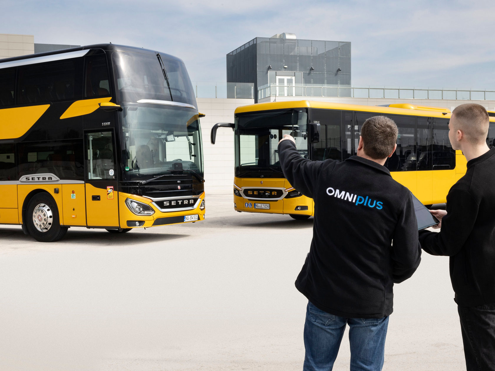 Doi angajați de service OMNIplus în fața a două autobuze Setra galbene în depozit