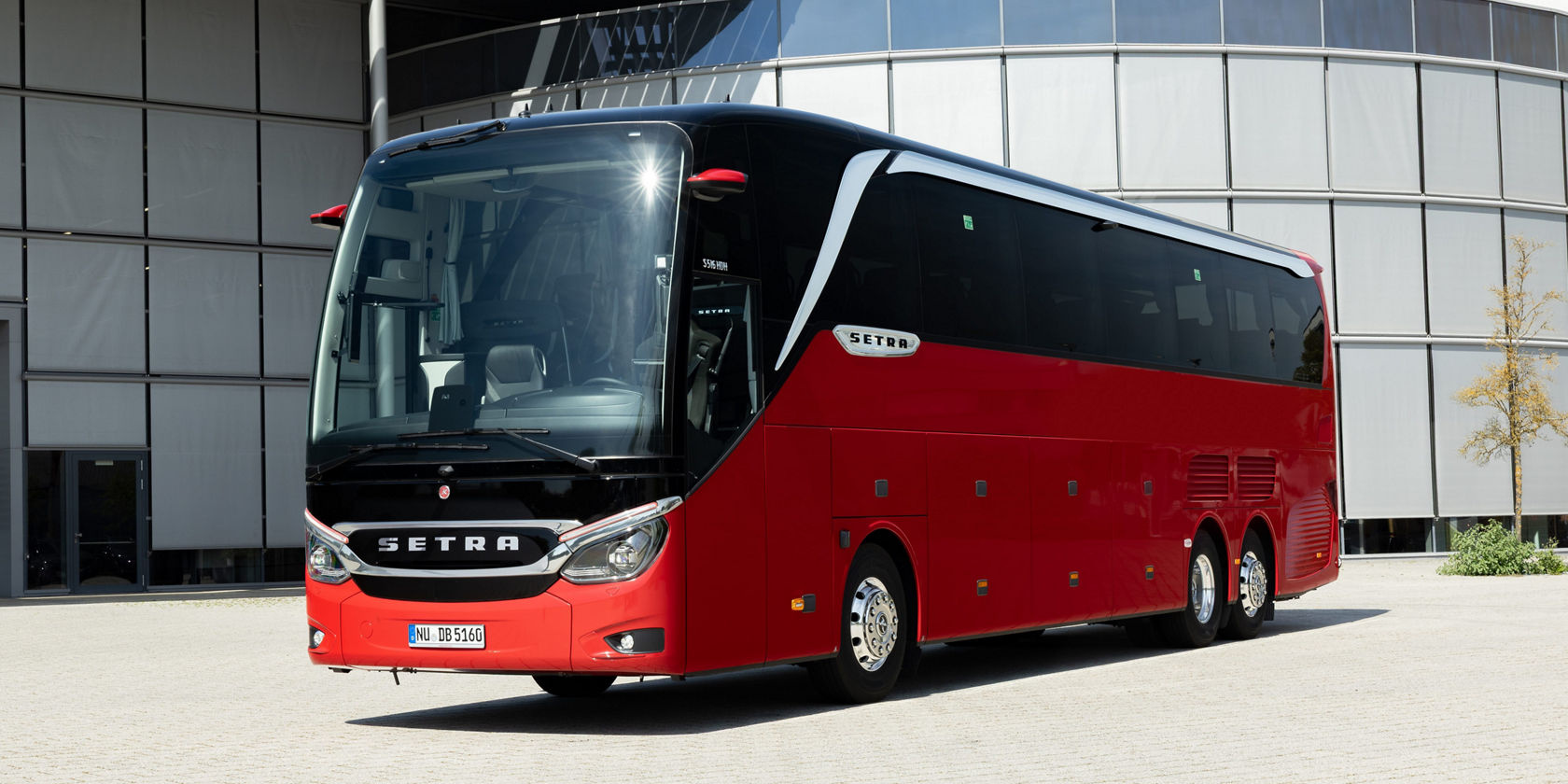 Autobus da turismo Setra Topclass rosso davanti alla facciata in vetro, vista laterale e scritta frontale SETRA