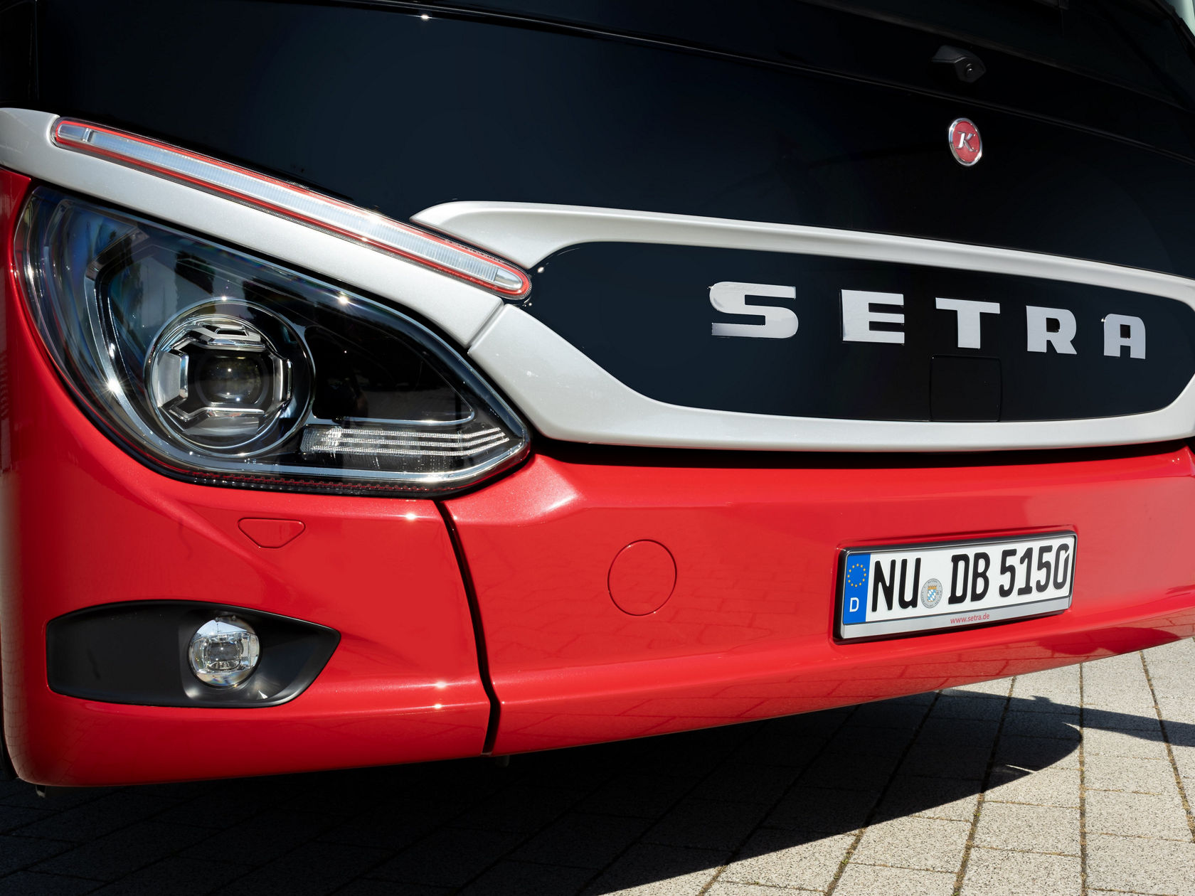 Imagem ampliada da frente de um autocarro de turismo Setra ComfortClass vermelho com faróis, grelha do radiador e inscrição Setra