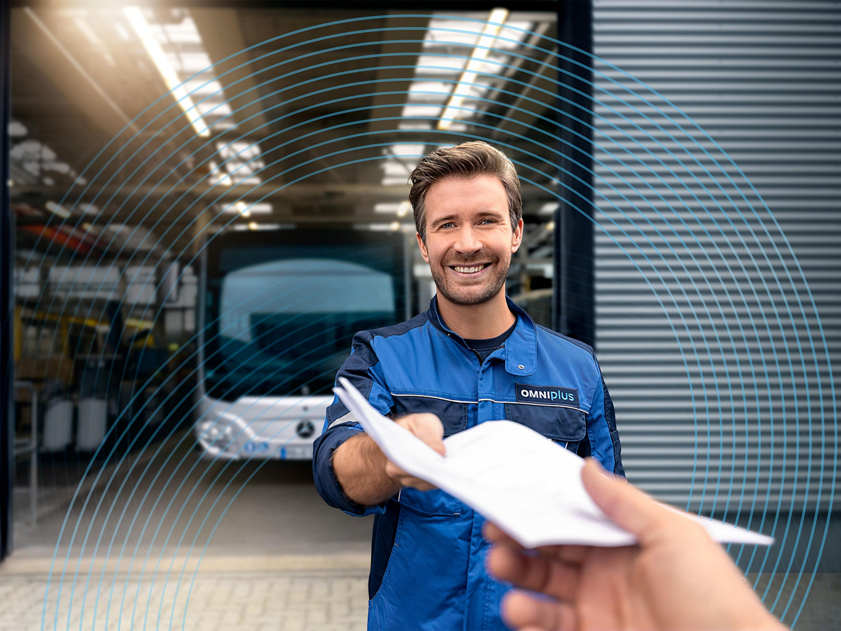 Pracownik serwisu w stroju roboczym OMNIplus przekazuje dokumenty przed warsztatem, w tle stoi autobus miejski Mercedes-Benz w hali zakładowej. 