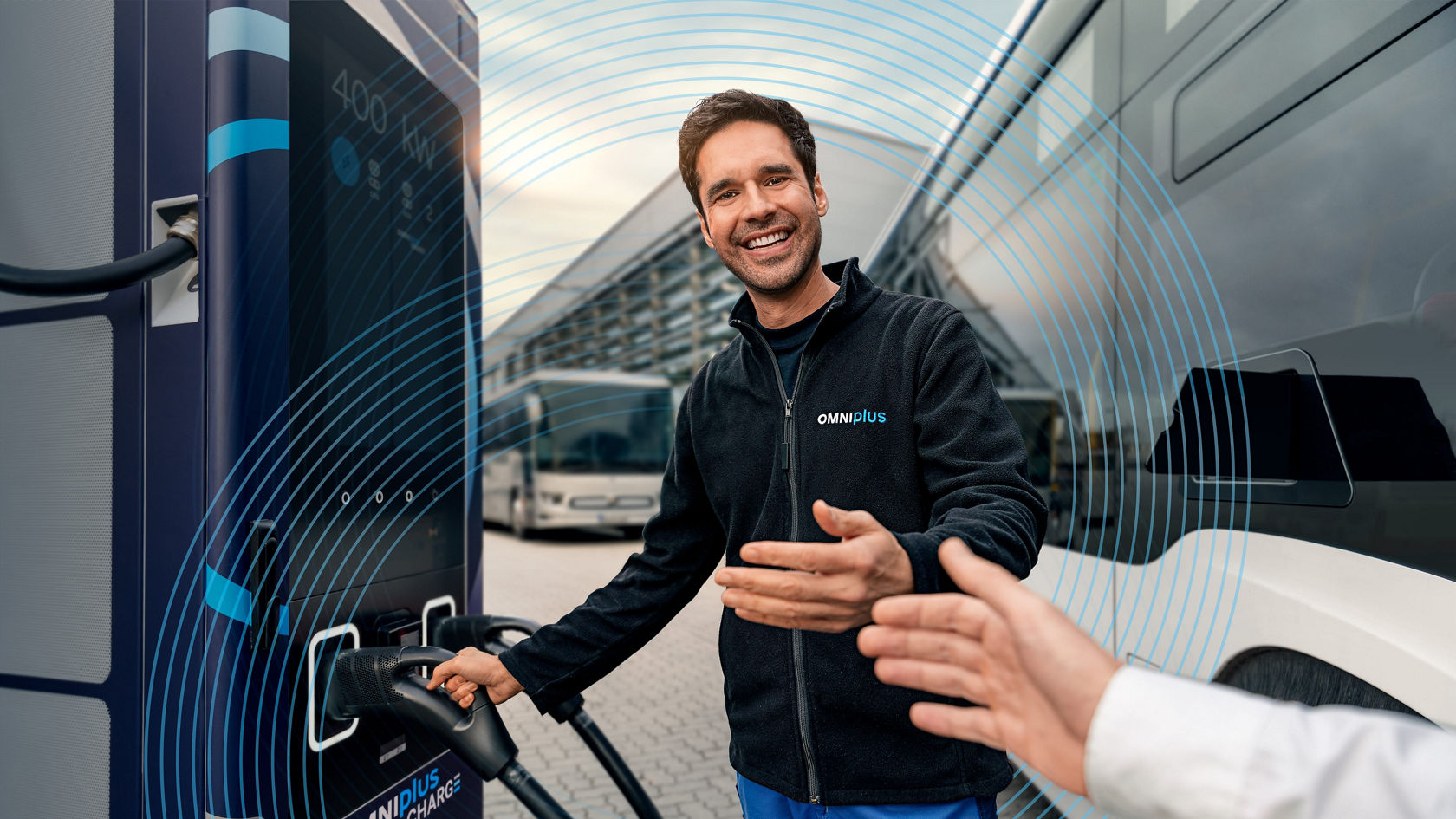 OMNIplus employee at OMNIplus CHARGE charging station, overlays charging cable into electric bus and greets customer with a handshake