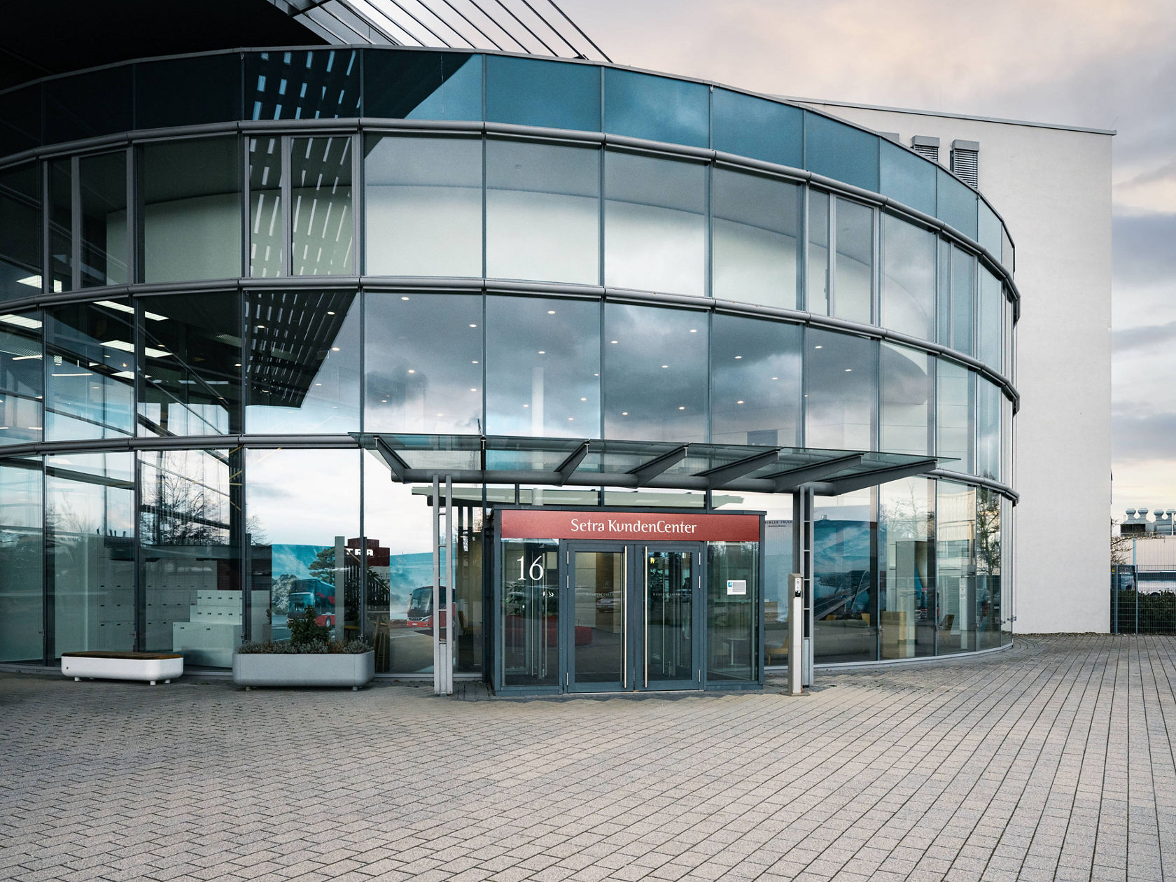 Area di ingresso del Centro Clienti Setra di Neu-Ulm con facciata in vetro rotonda e ingresso coperto